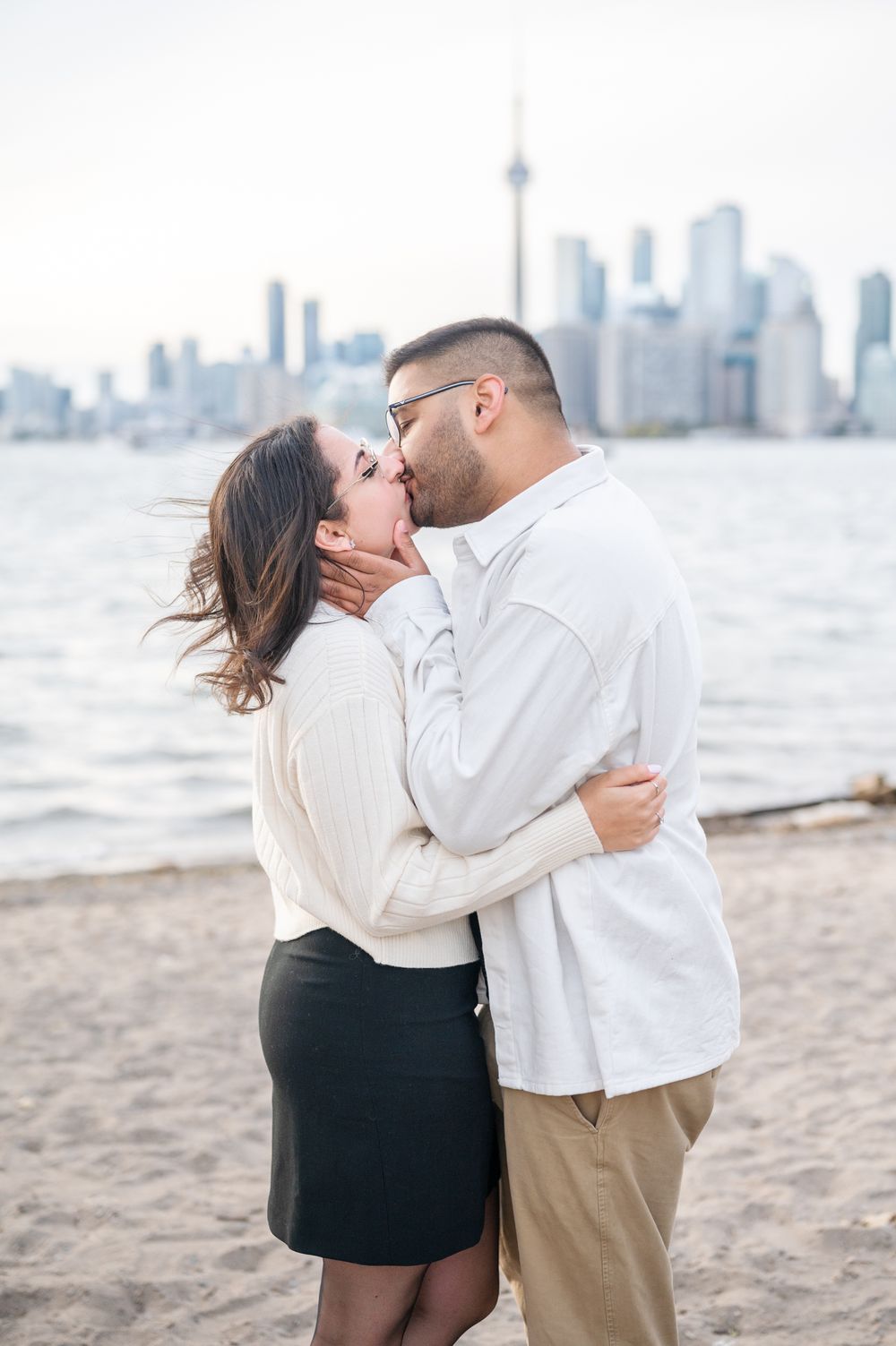 A couple shares a romantic engagement proposal on Toronto Island, with the iconic CN Tower and city skyline creating a stunning backdrop.