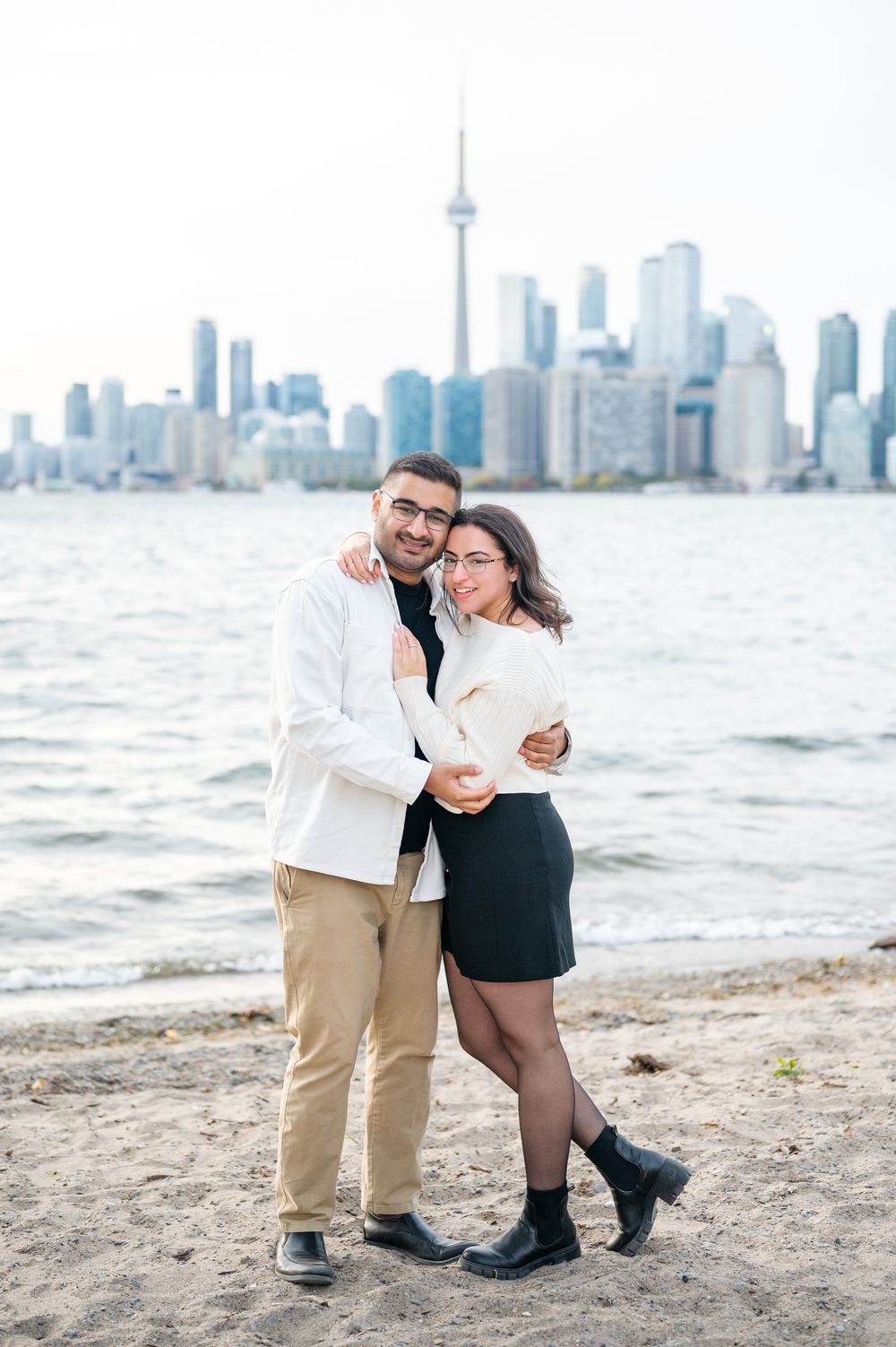 A couple shares a romantic engagement proposal on Toronto Island, with the iconic CN Tower and city skyline creating a stunning backdrop.