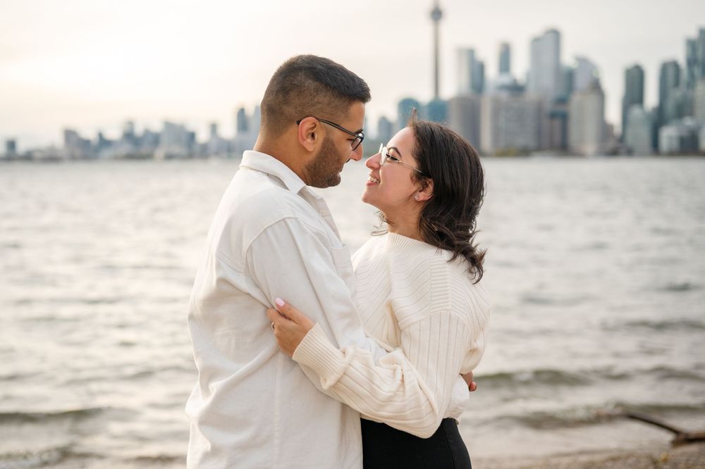 A couple shares a romantic engagement proposal on Toronto Island, with the iconic CN Tower and city skyline creating a stunning backdrop.