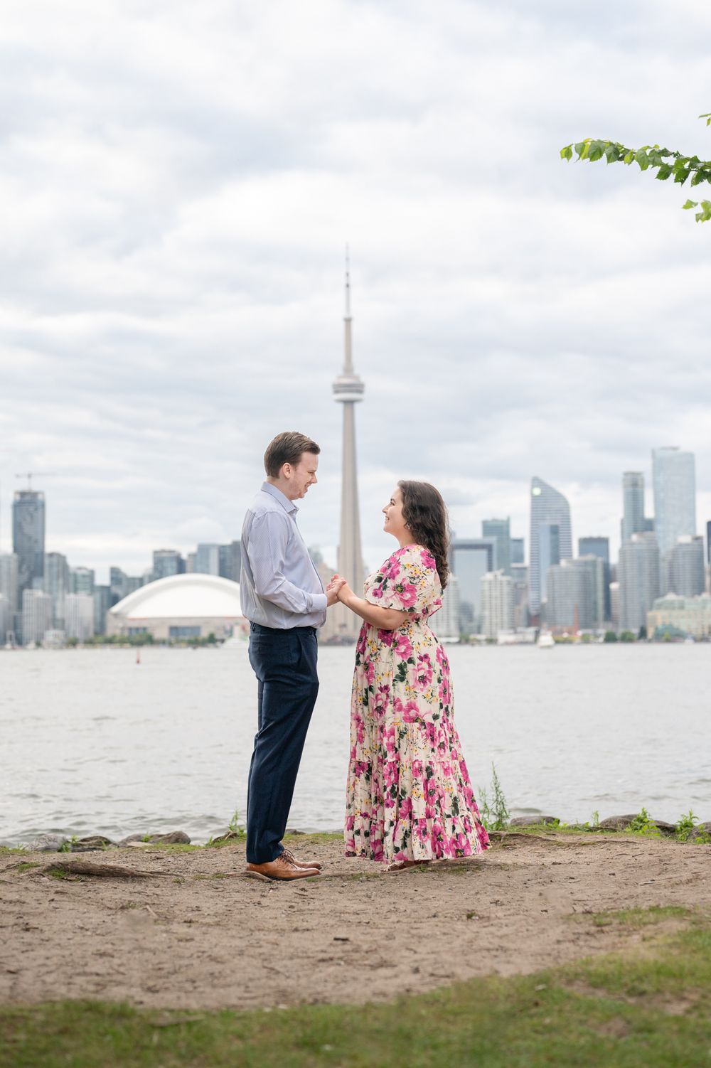 A couple shares a romantic engagement proposal on Toronto Island, with the iconic CN Tower and city skyline creating a stunning backdrop.