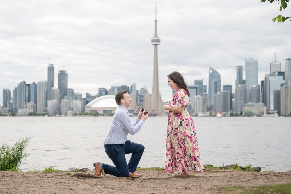 A couple shares a romantic engagement proposal on Toronto Island, with the iconic CN Tower and city skyline creating a stunning backdrop.