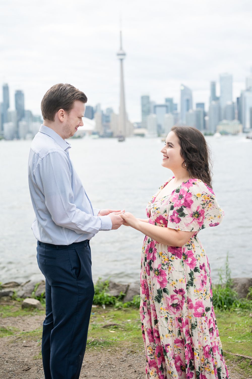 A couple shares a romantic engagement proposal on Toronto Island, with the iconic CN Tower and city skyline creating a stunning backdrop.