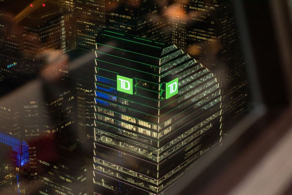 Illuminated office building with green glowing TD sign on top viewed at night from above.