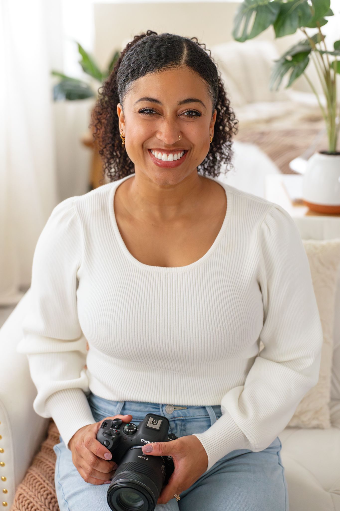 Woman in a pink ruffled sweater sits on a couch and smiles warmly.