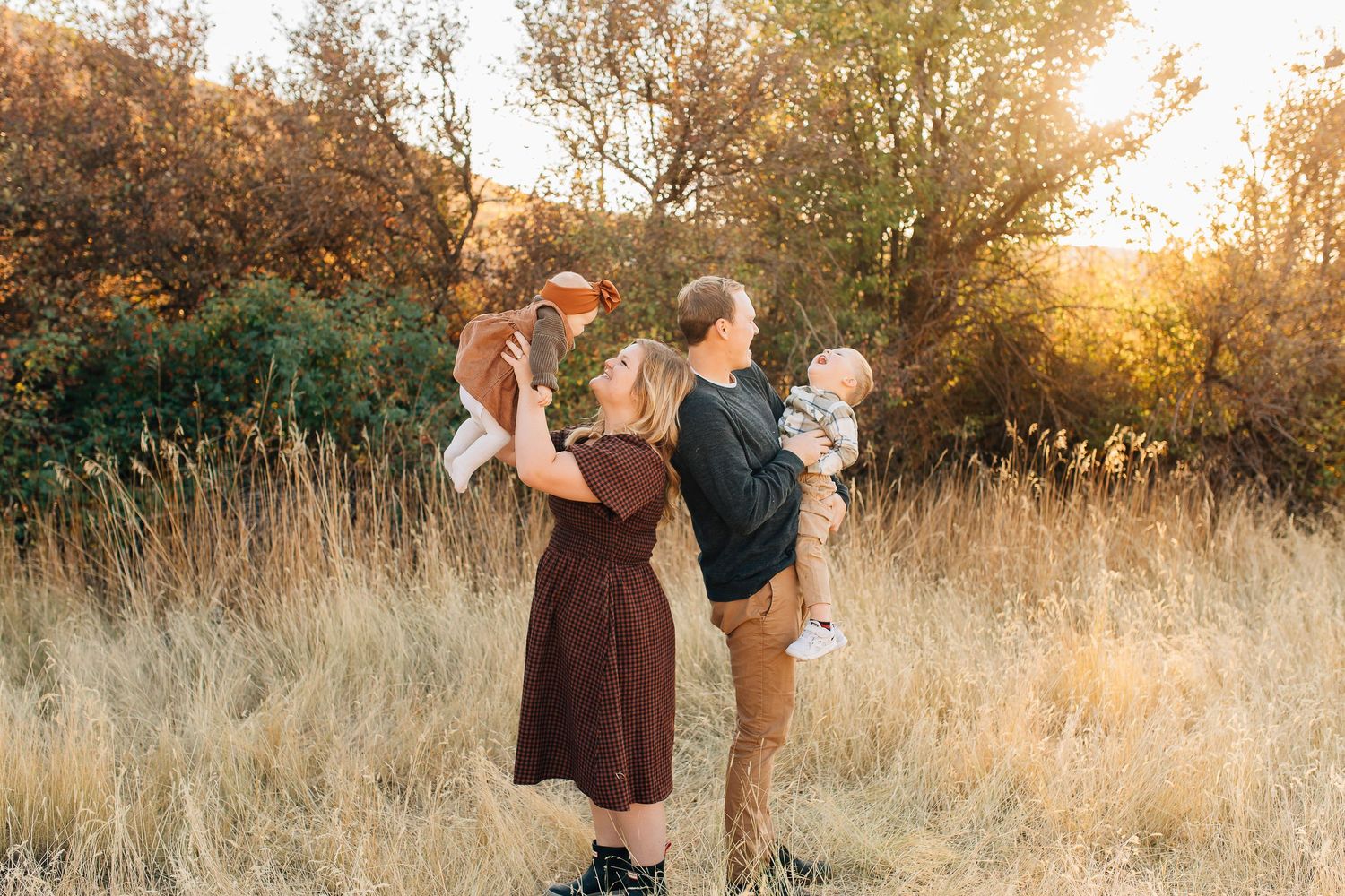 A family plays together in a sun-drenched field of tall grass during a golden autumn sunset.