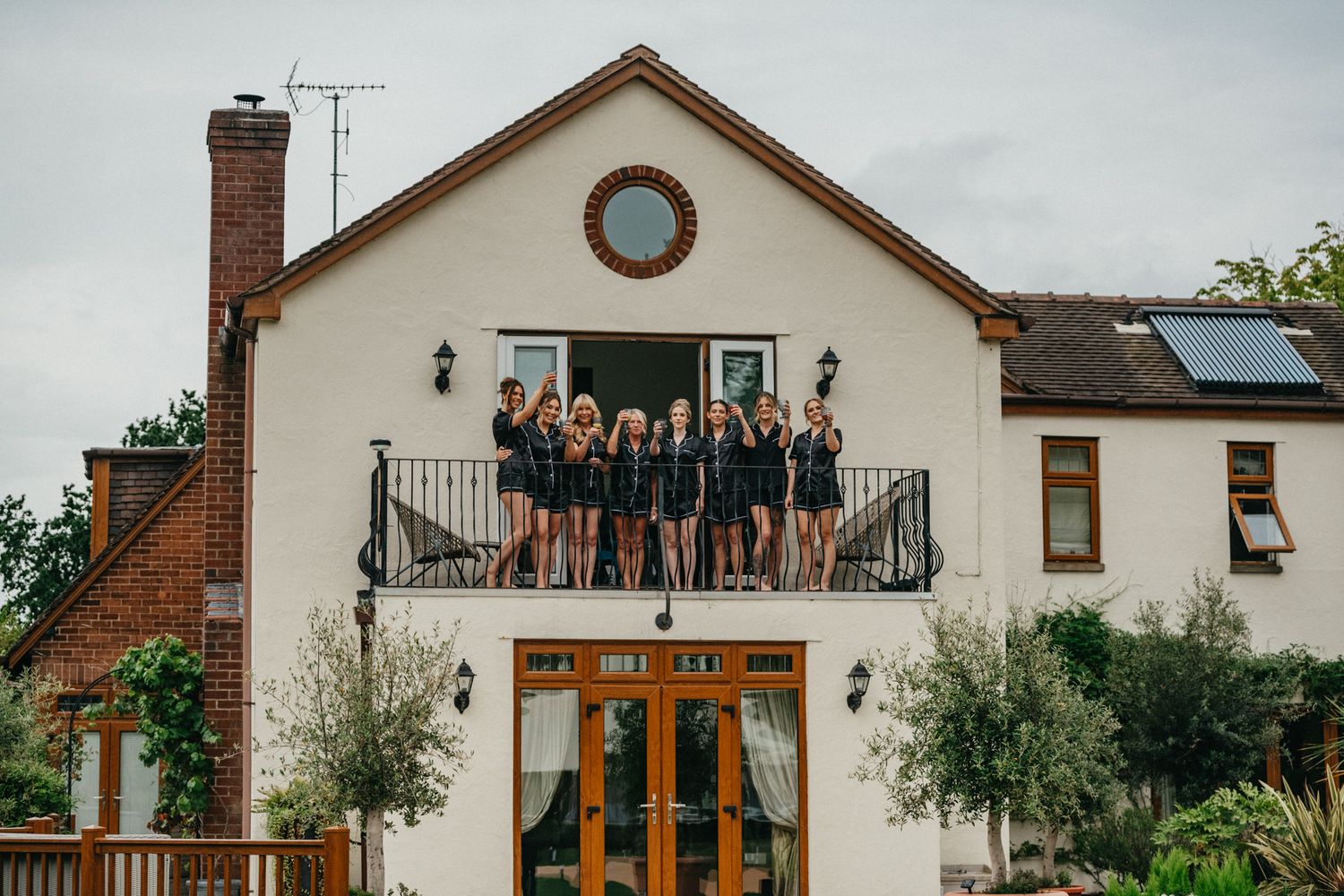 Large white house with brick accents and balcony where people are gathered.