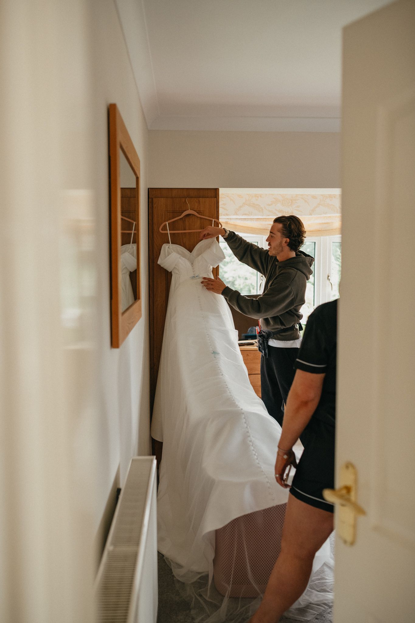 Wedding dress being hung and prepared in a bright, neutral-toned room.