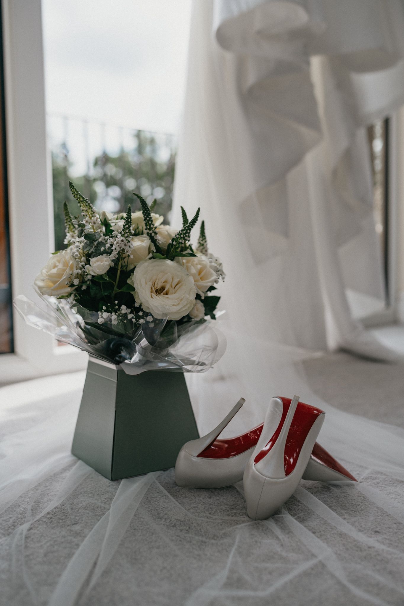 White bridal shoes and floral arrangement displayed on light surface.