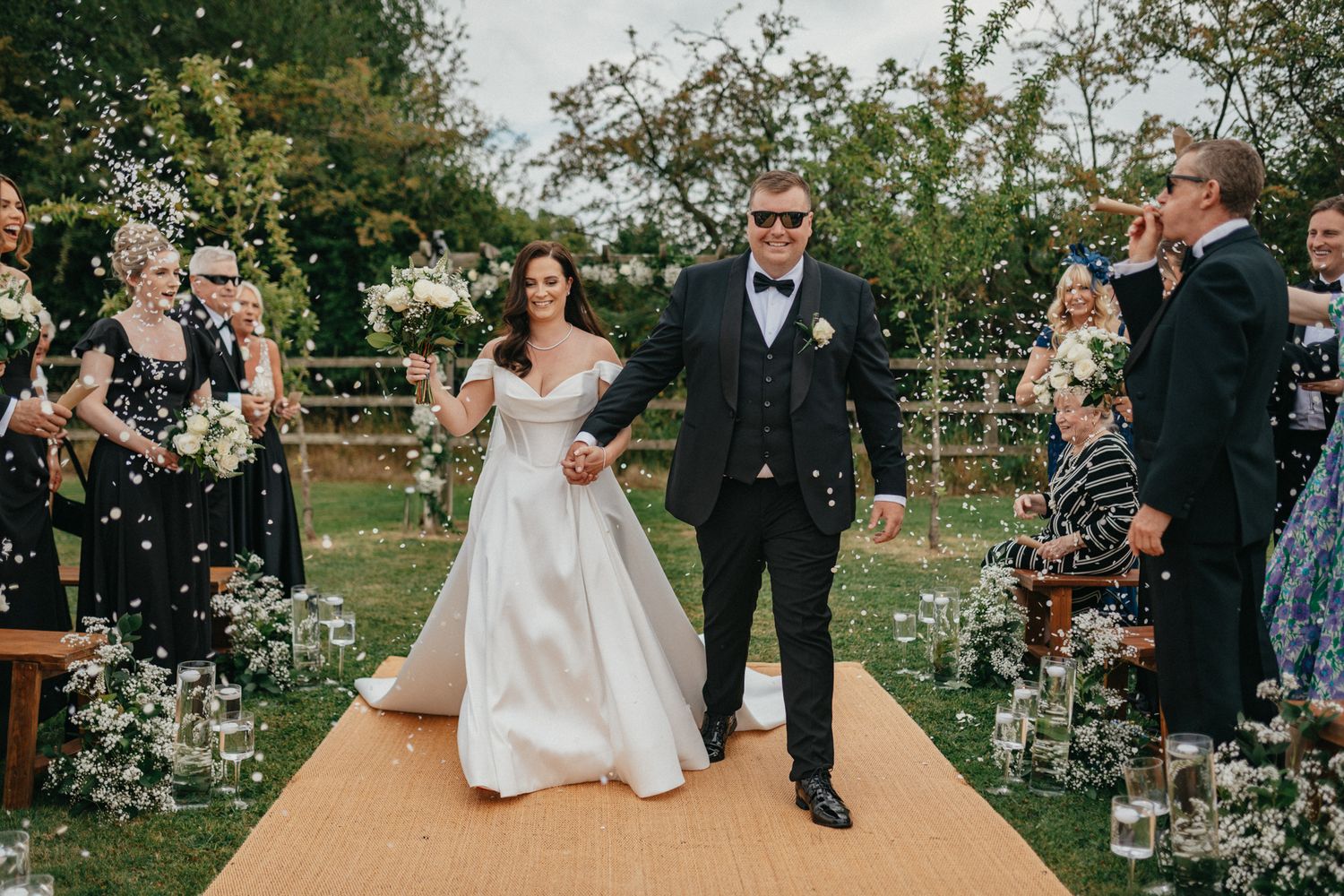 Newlyweds walk down the aisle while guests throw flower petals in celebration.