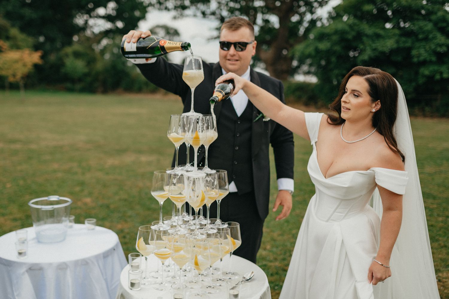 A champagne tower being filled at an outdoor wedding reception.