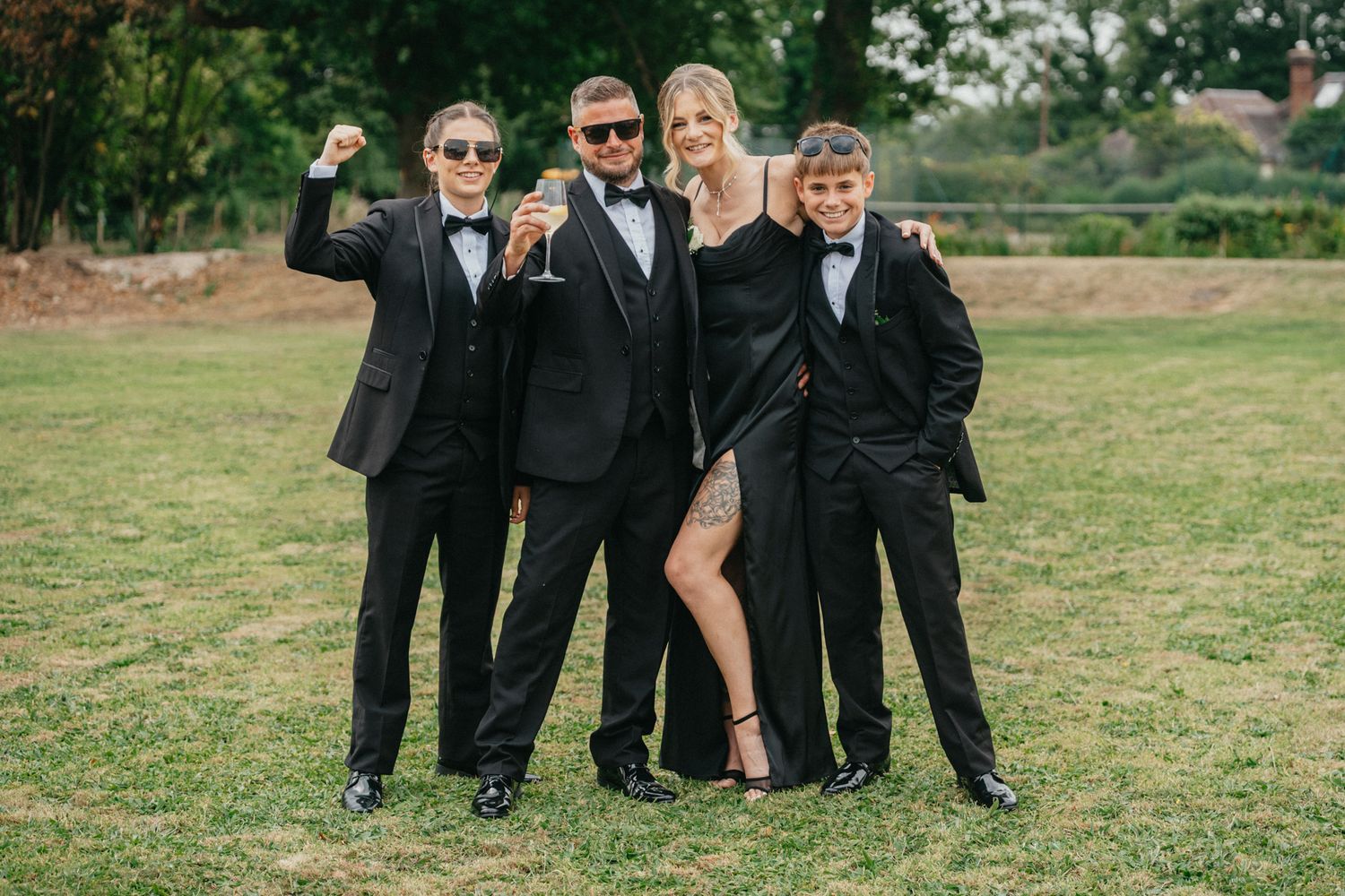 Group in formal attire poses together on grass for stylish wedding photo.