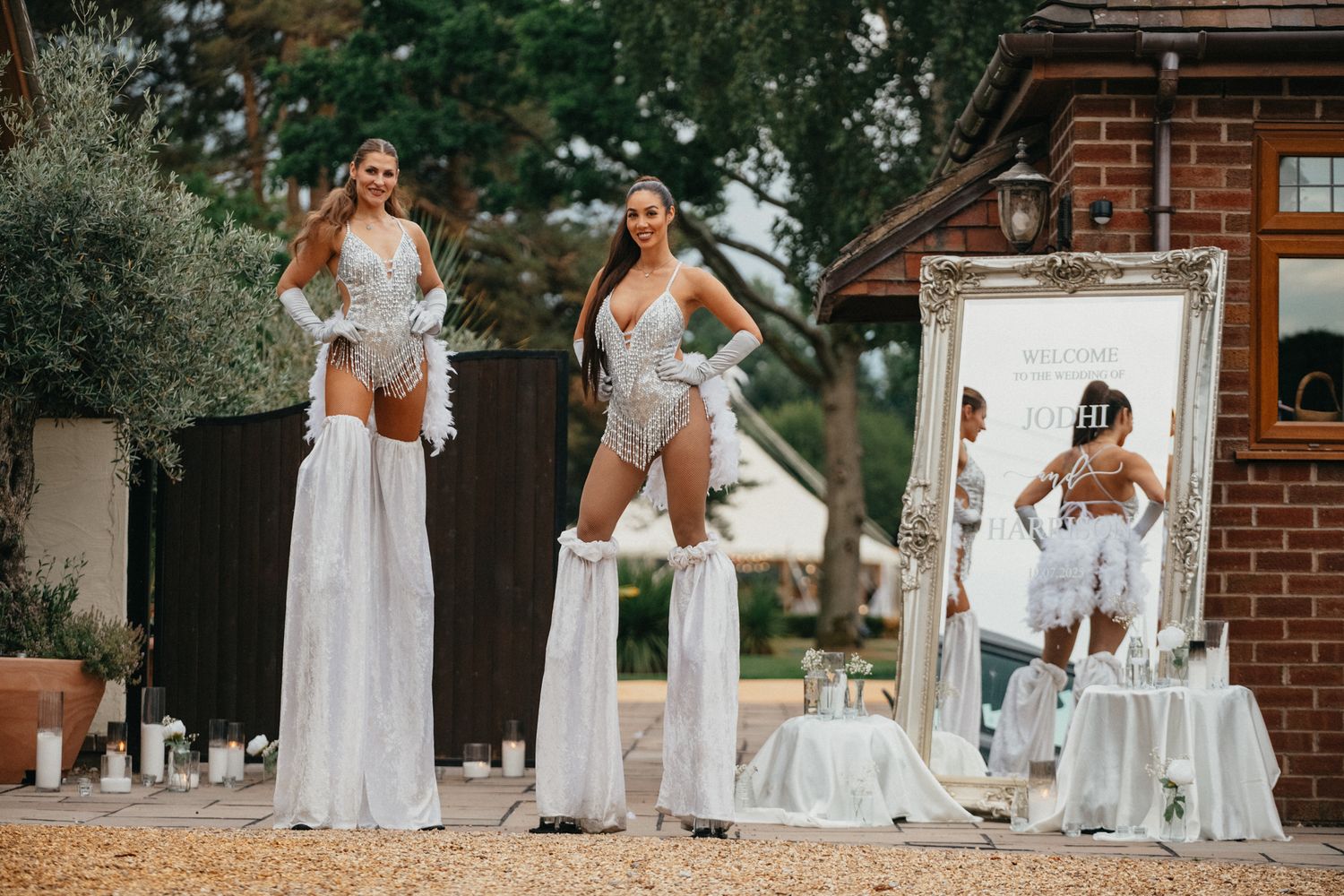 Two performers in white outfits pose on stilts during outdoor entertainment show.