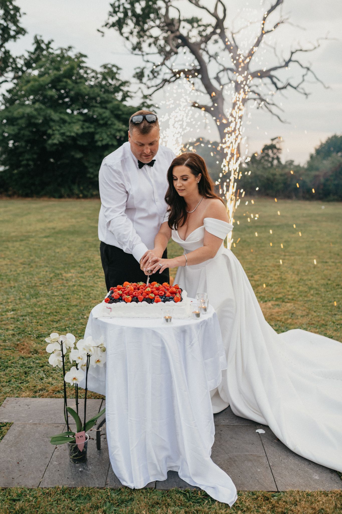Couple cuts their wedding cake at an outdoor reception with string lights.