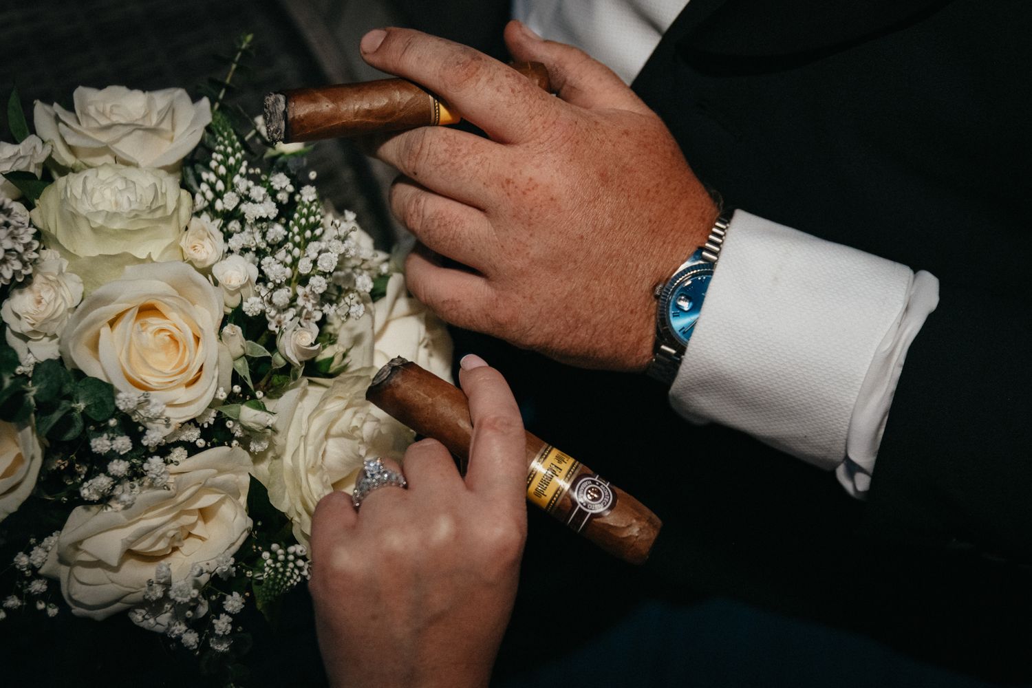 Close-up of hands with rings and white rose bouquet details.