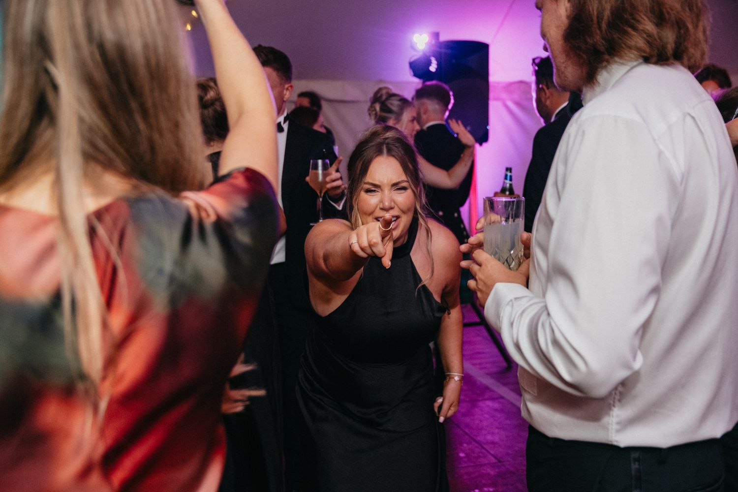 Wedding guests dancing together on a dimly lit dance floor with purple ambient lighting.