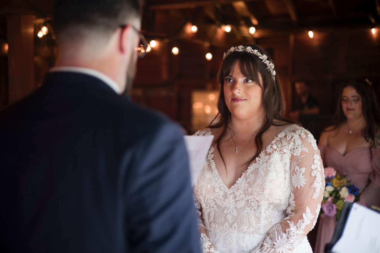 A couple exchanges vows during an indoor wedding ceremony with string lights and romantic ambiance in the background.