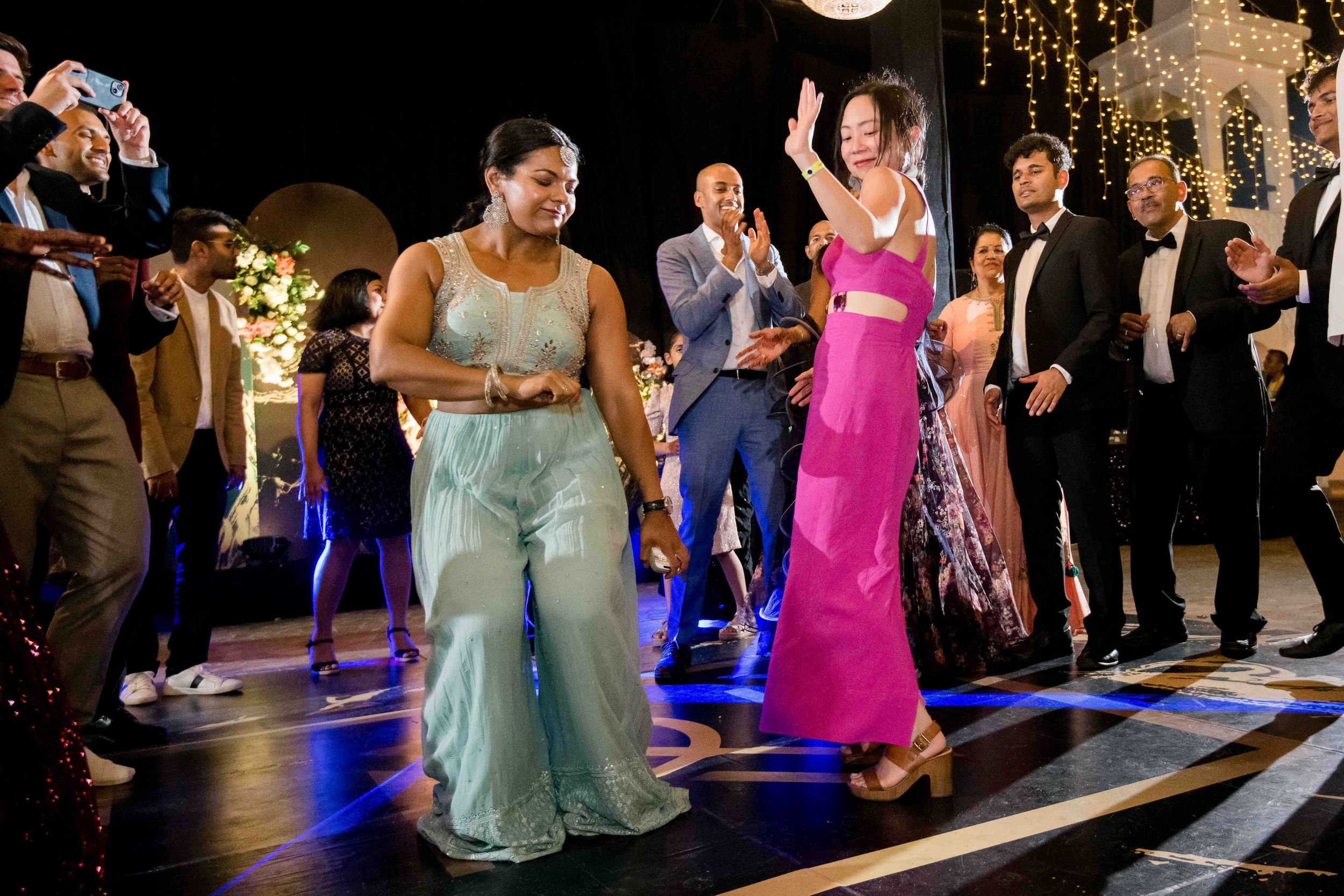 People dancing and celebrating at a nighttime party on a light-up floor with festive decorations.