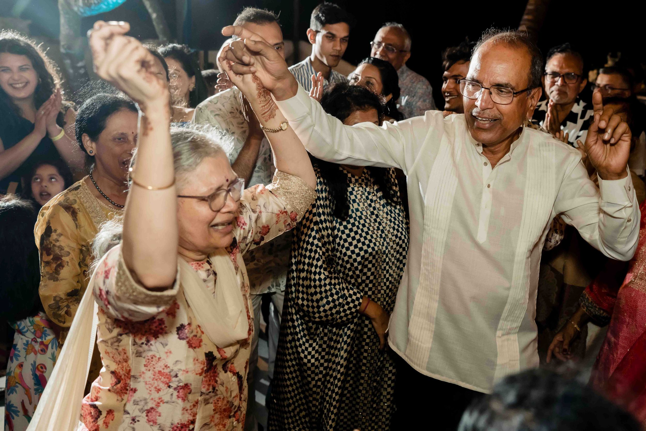 Wedding guests dance enthusiastically with raised arms at a reception party filled with joyful energy.