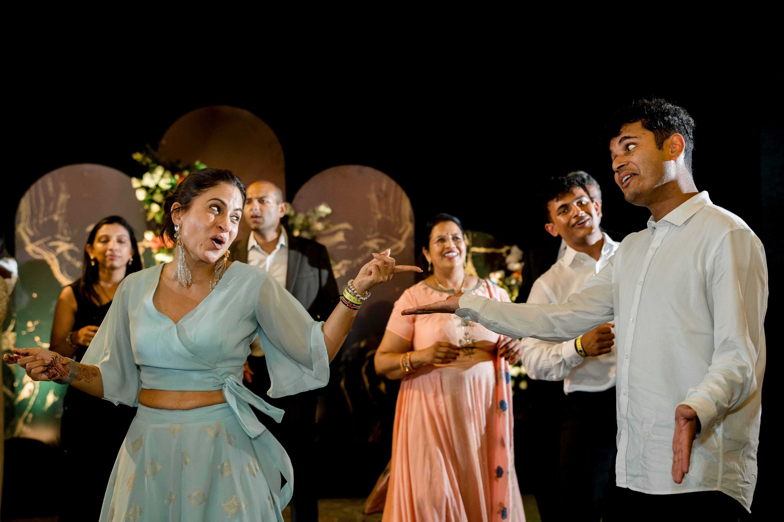 Party guests interact and dance on a dimly lit dance floor during what appears to be a wedding reception.