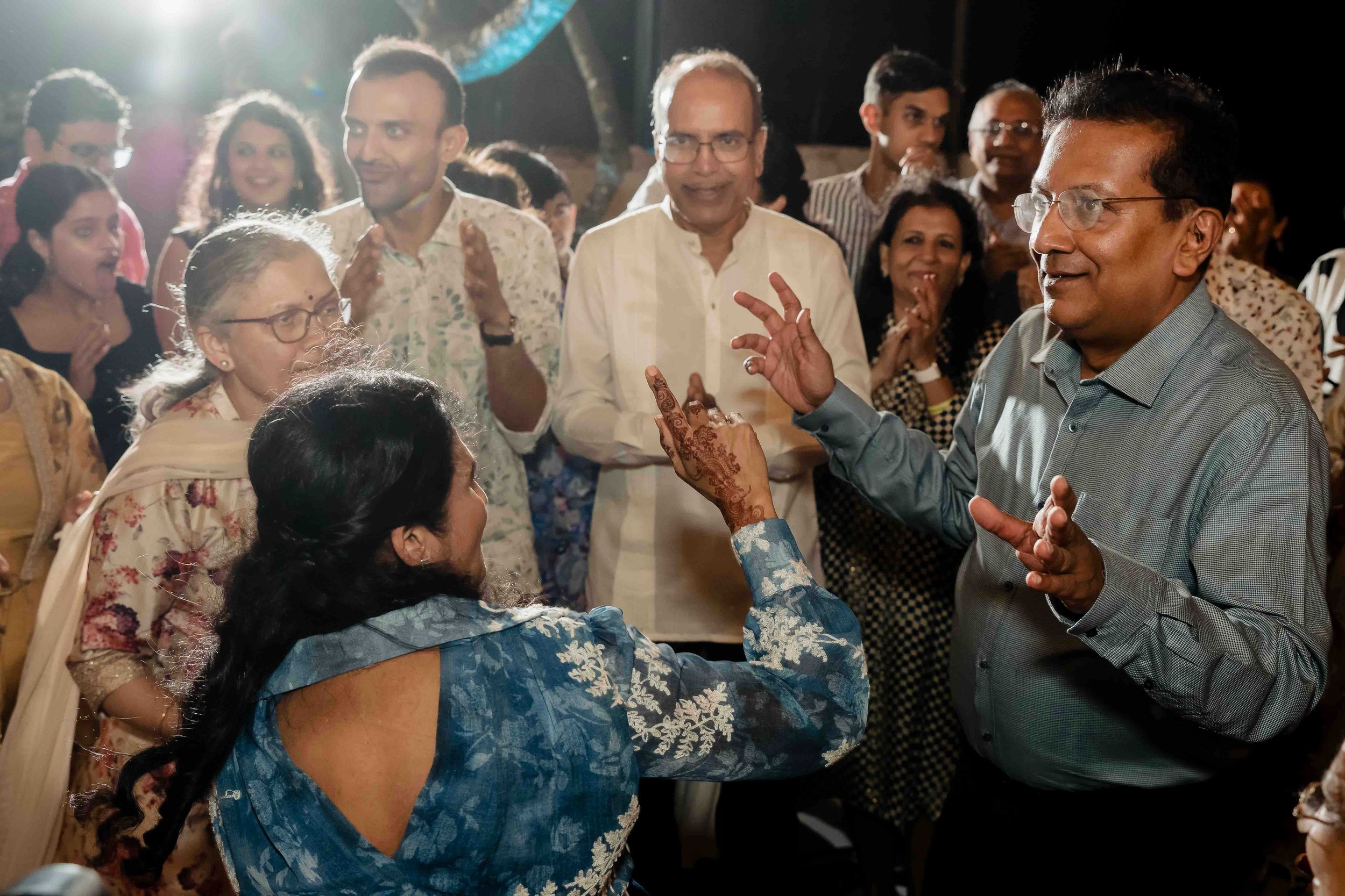 A lively reception event shows people engaged in conversation and dancing with joyful expressions on a dark-lit dance floor.