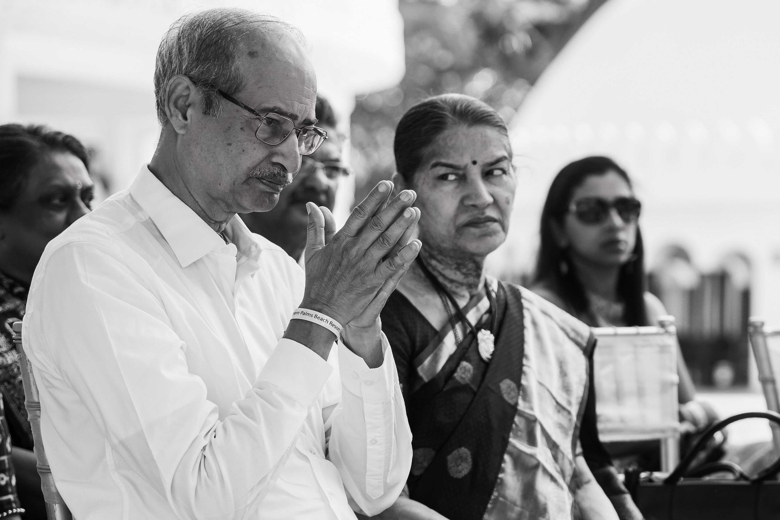 Two suit-clad men in discussion at an outdoor event, with one individual gesturing while speaking in black and white.