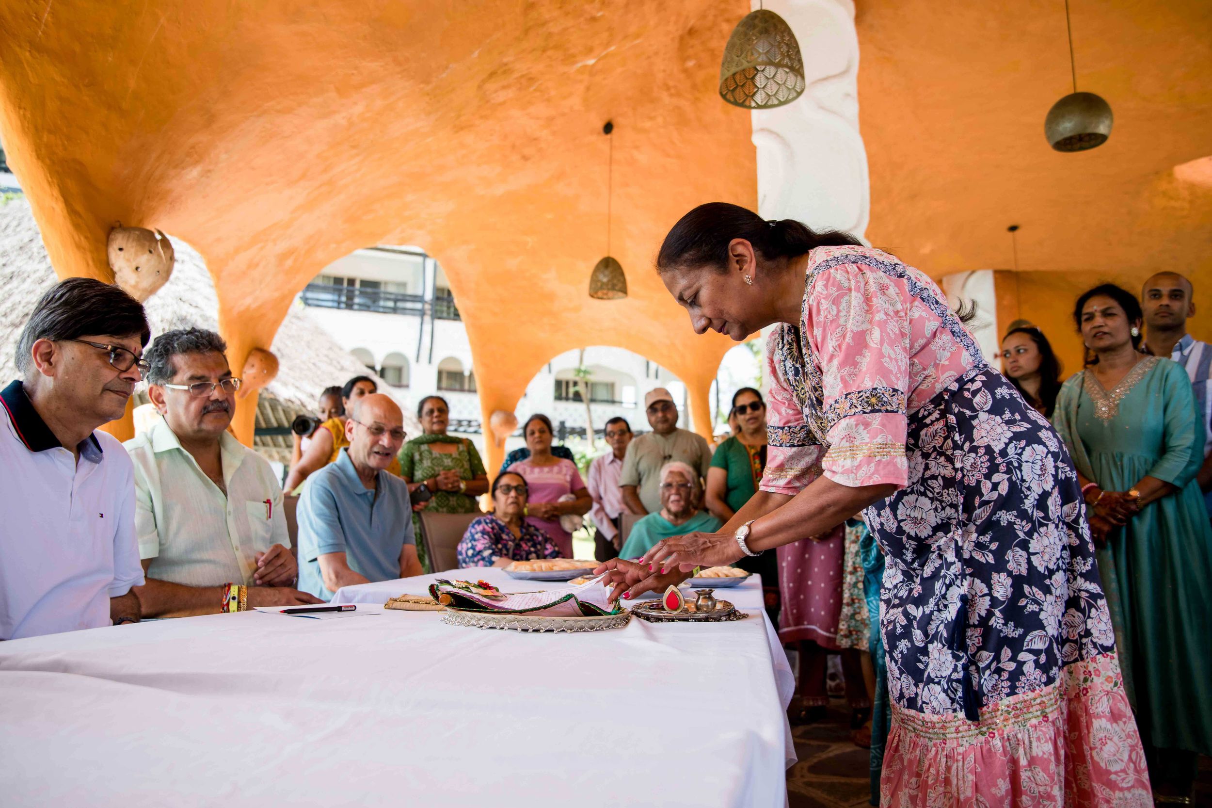 Guests gather around a long table under an orange-colored ceiling during a social gathering.