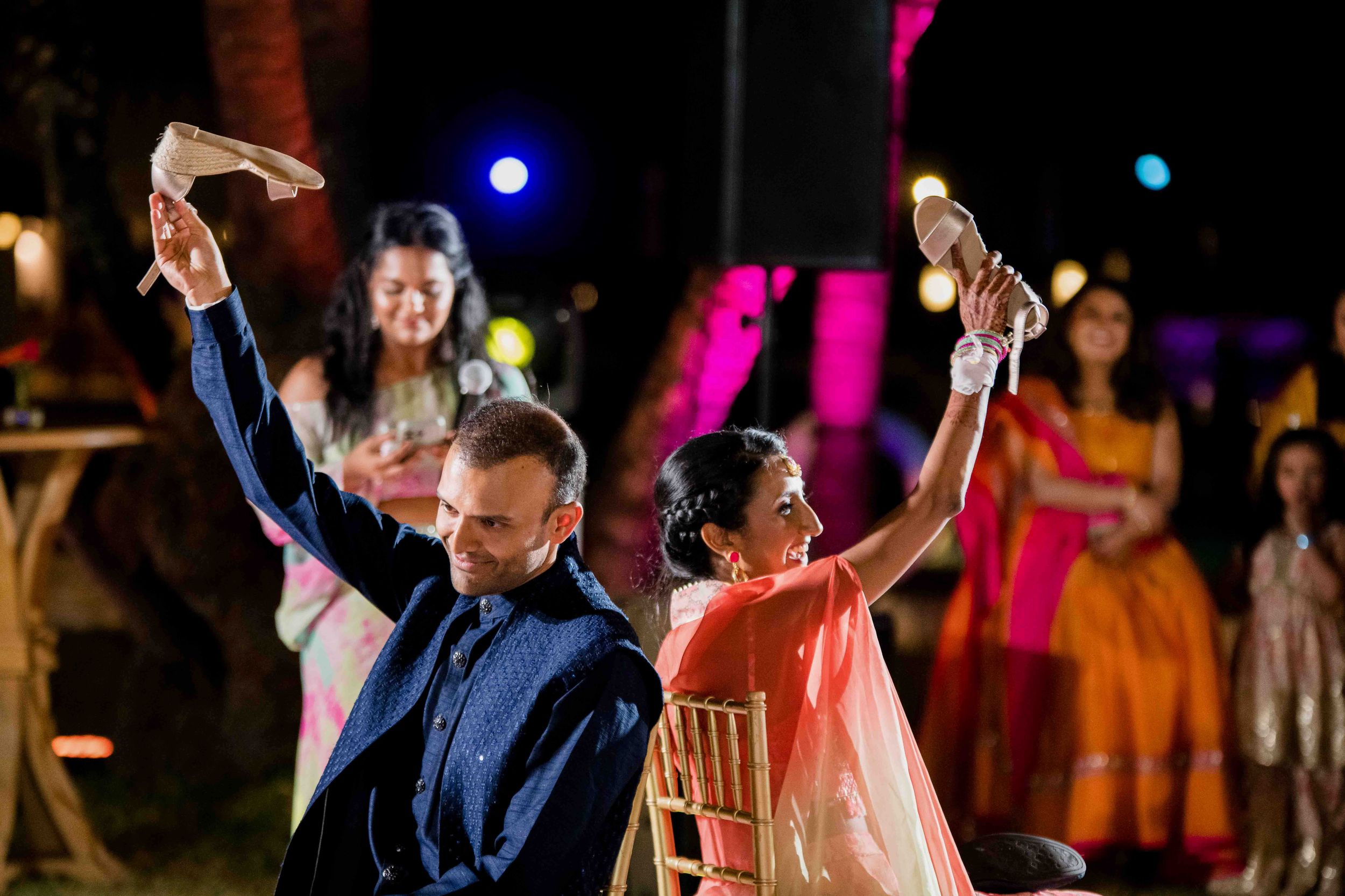 Newly married couple dances during their first dance at a wedding reception with colorful lights in background.