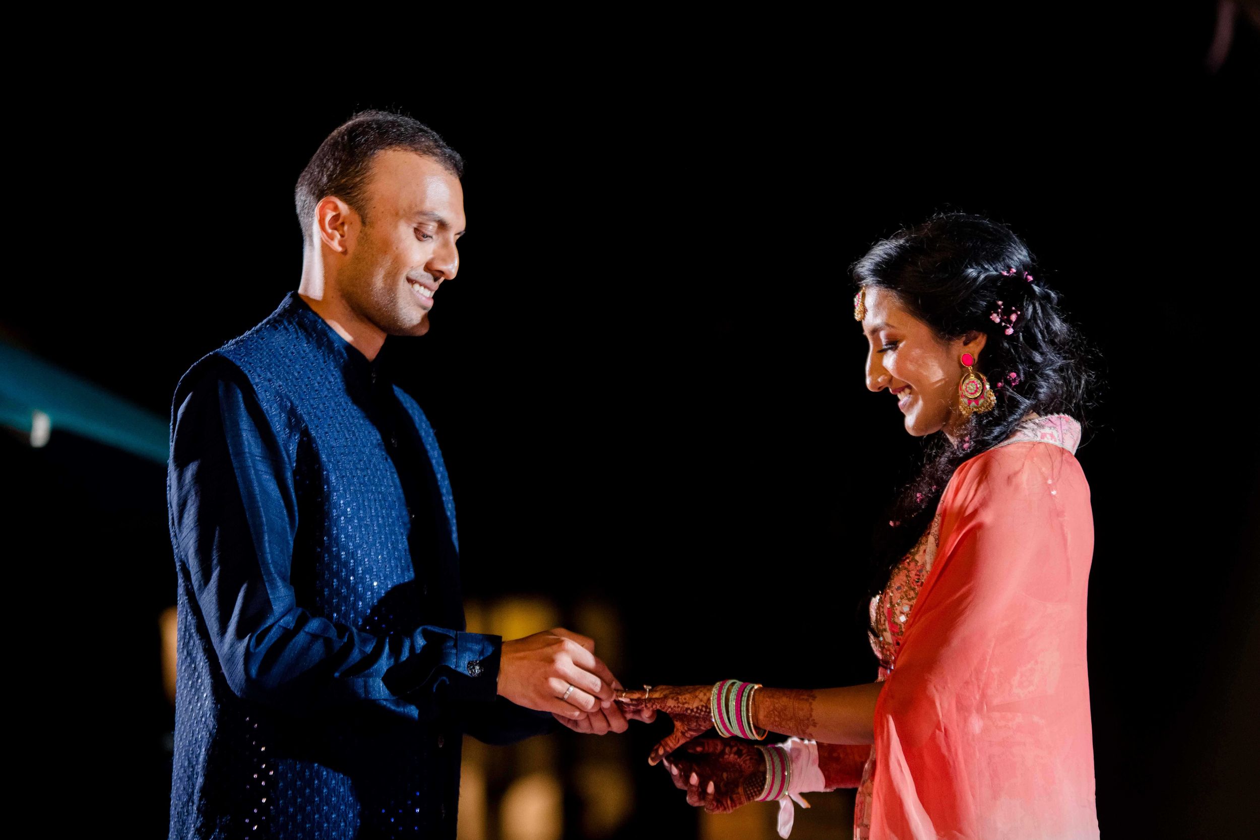 A person in a blue suit and another in a bright pink dress stand together on a darkened stage.