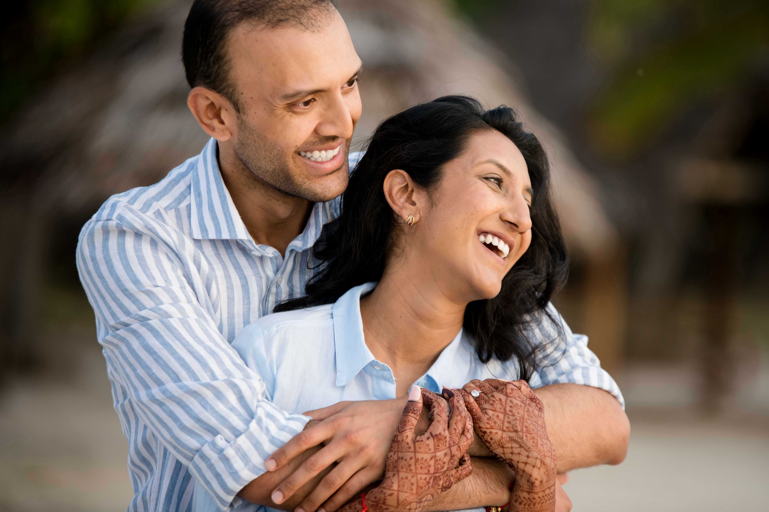 A happy couple embraces and laughs together outdoors with warm lighting and blurred natural background.