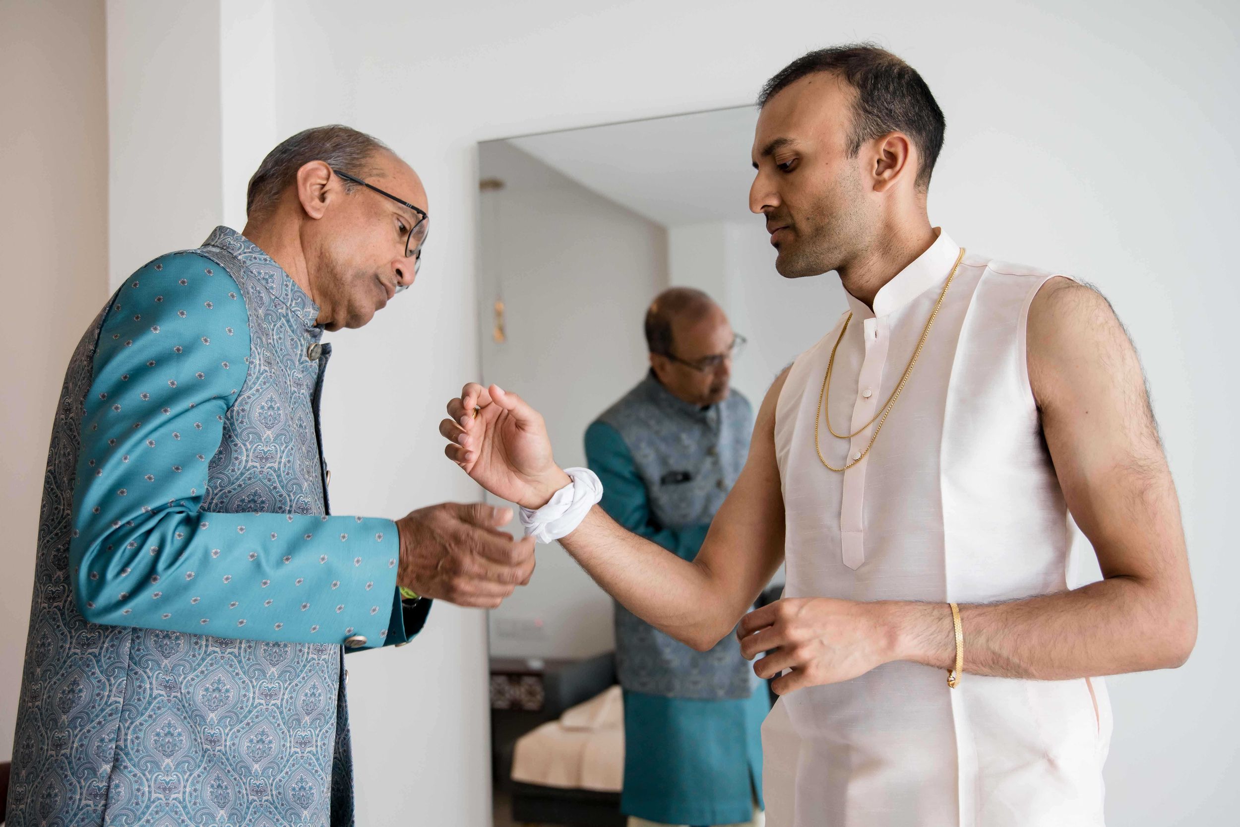 Two people in a room shake hands as a third person stands in the background.