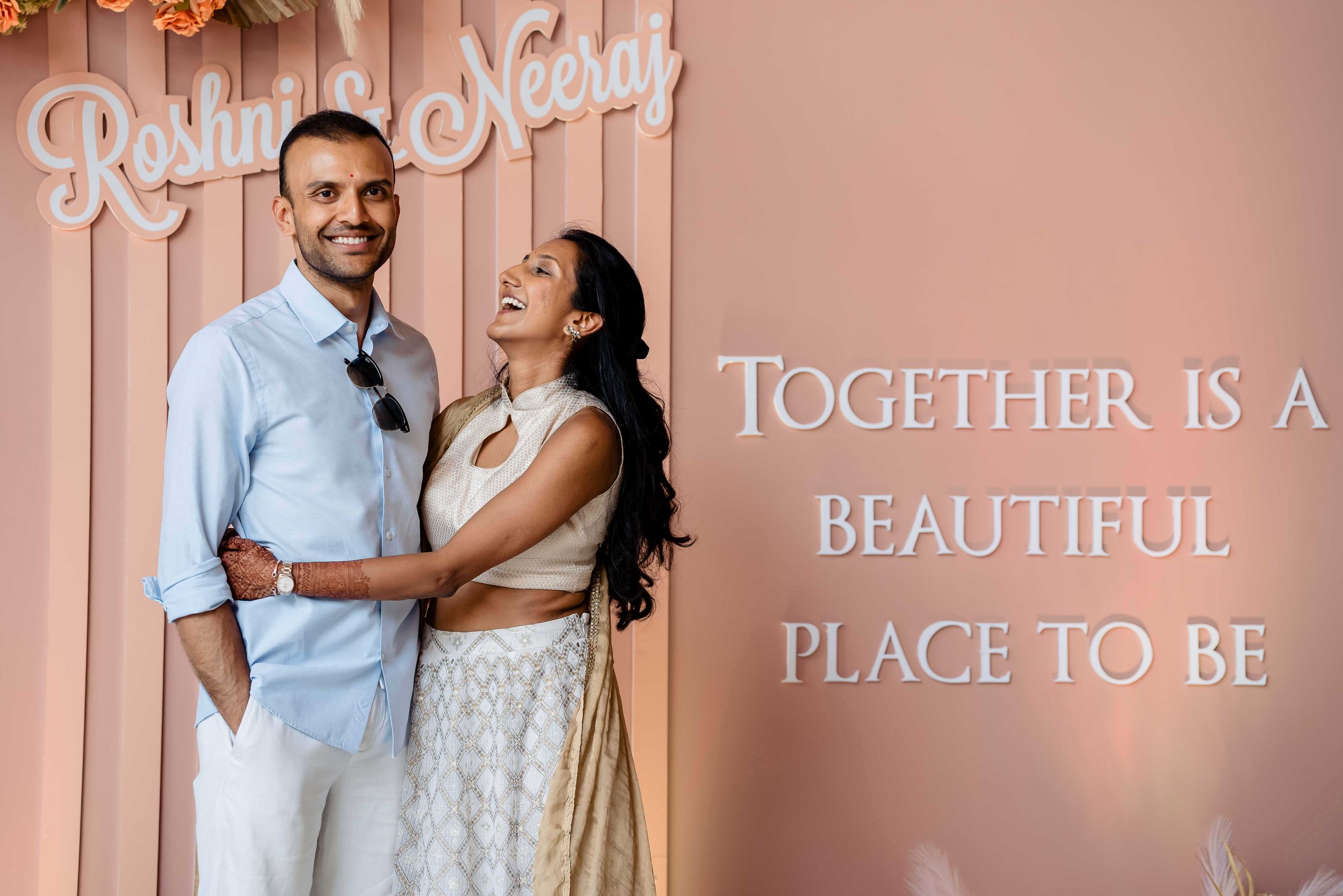 A couple embraces in front of a pink wall with text that reads Together is a Beautiful Place to Be.