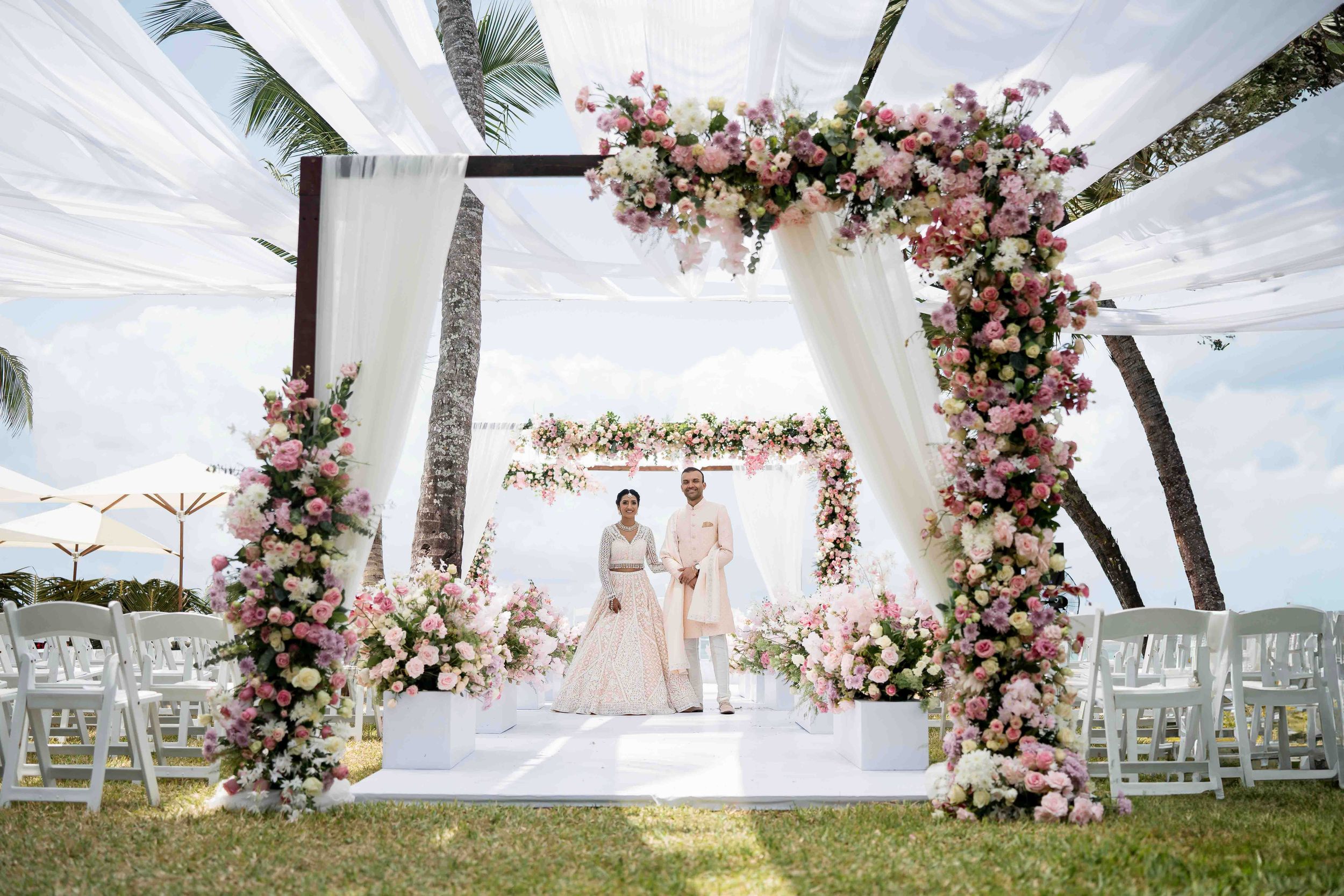 A beachside wedding ceremony setup with white chairs and pink floral arch decorations overlooking the ocean.