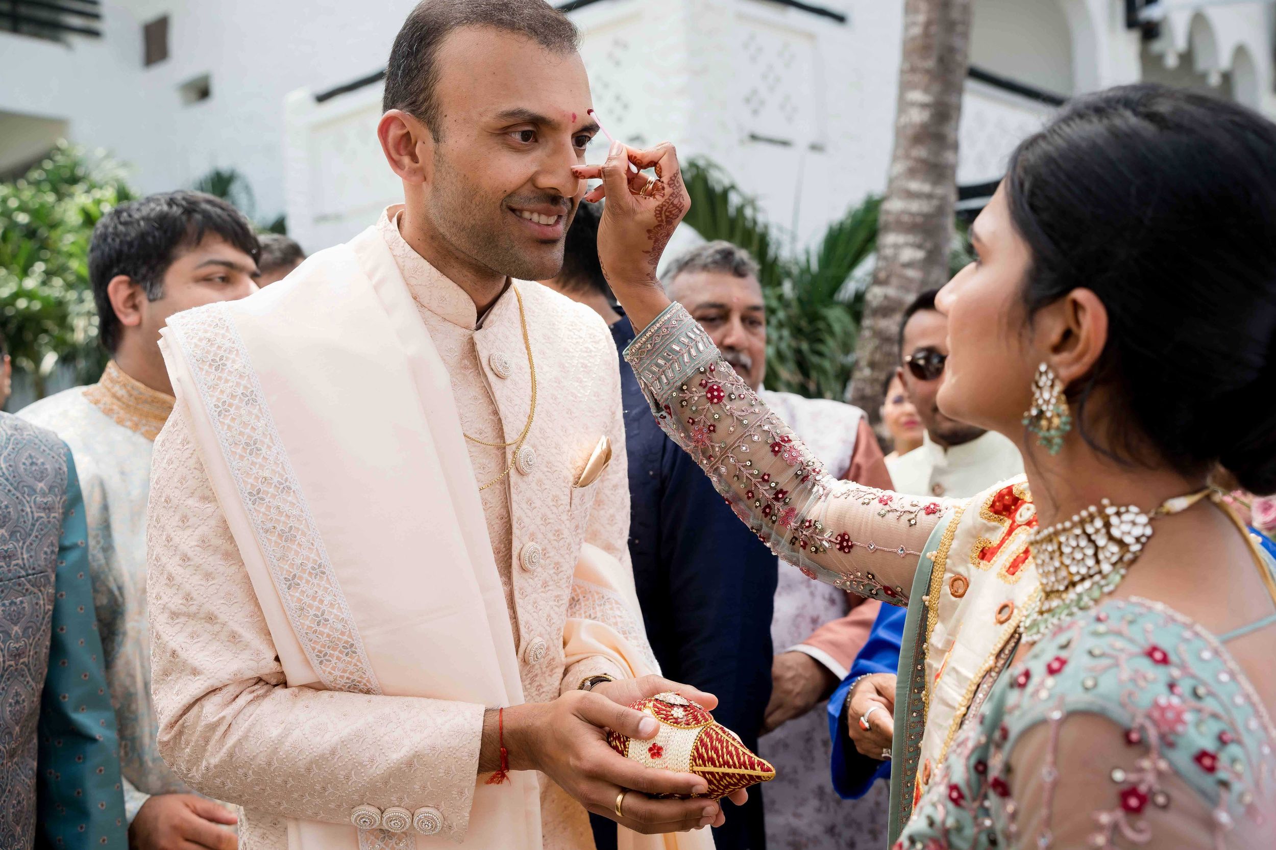 A couple shares a lighthearted moment at a gathering as they interact with each other wearing traditional wedding attire.