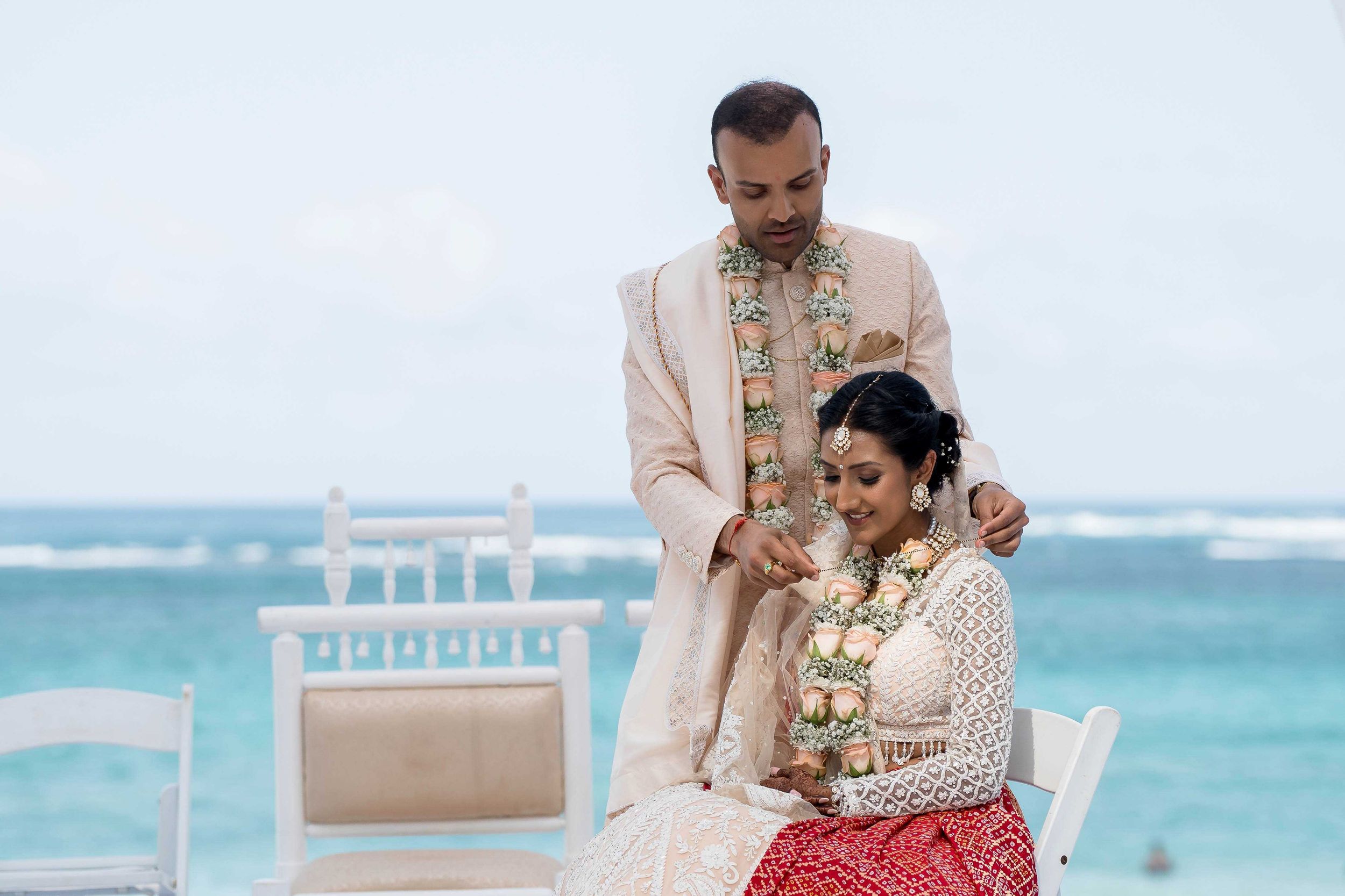 A beige and gold Indian wedding ceremony setup on a tropical beach with turquoise waters in the background.