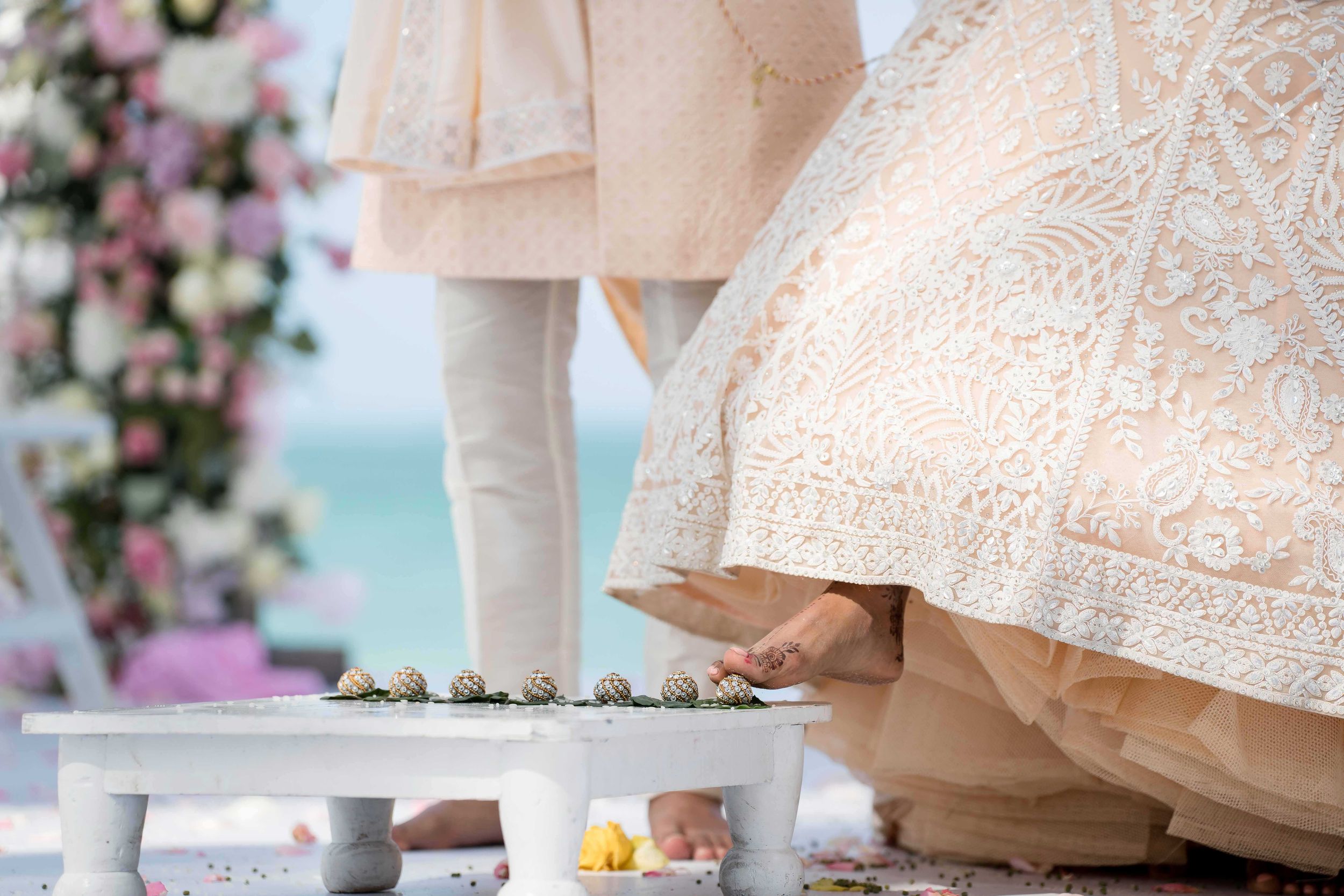 Elegant wedding cake with intricate lace details and floral decorations displayed at an indoor reception venue.