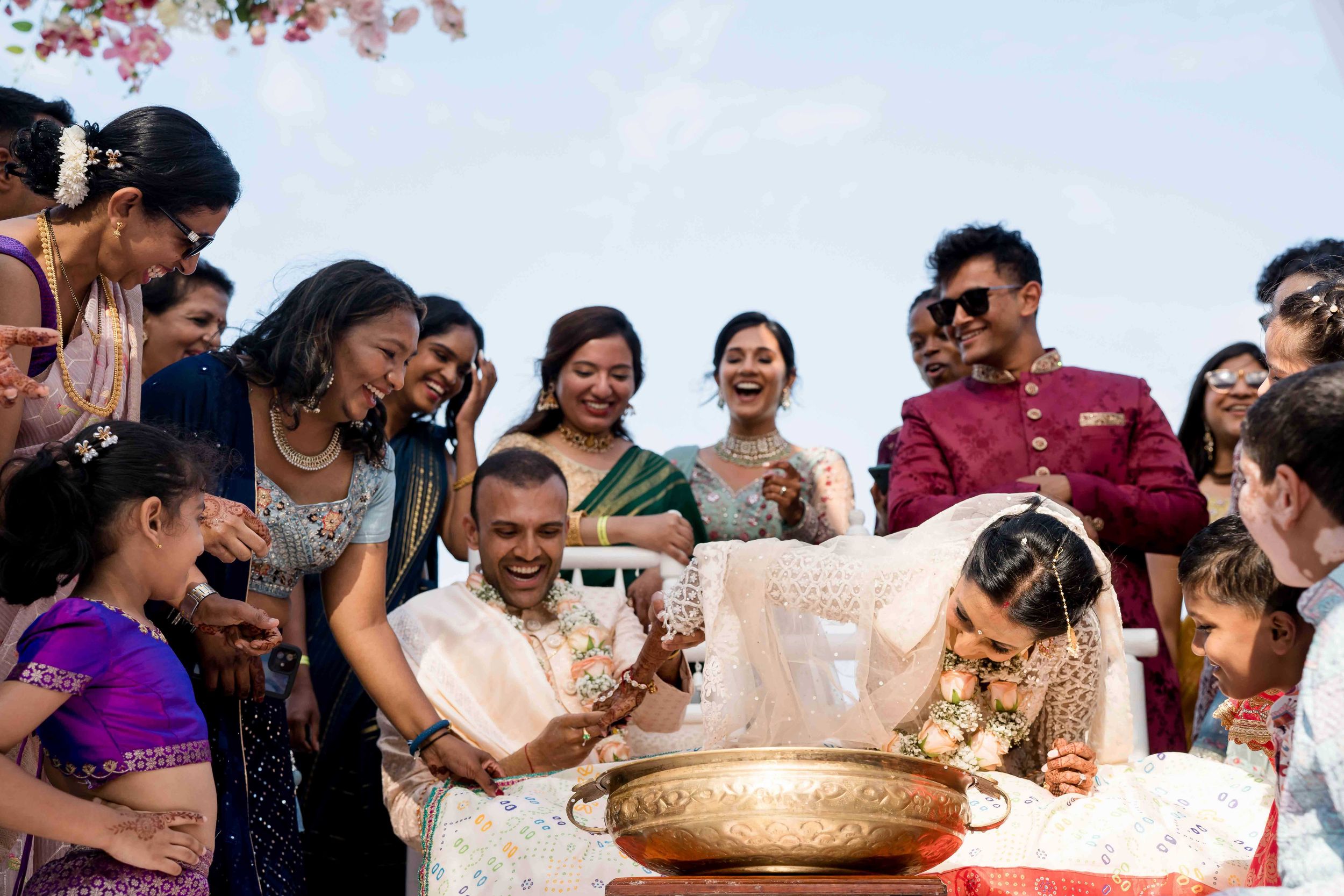 A colorful Indian wedding ceremony takes place with guests gathered around ceremonial items and decorations on a table.