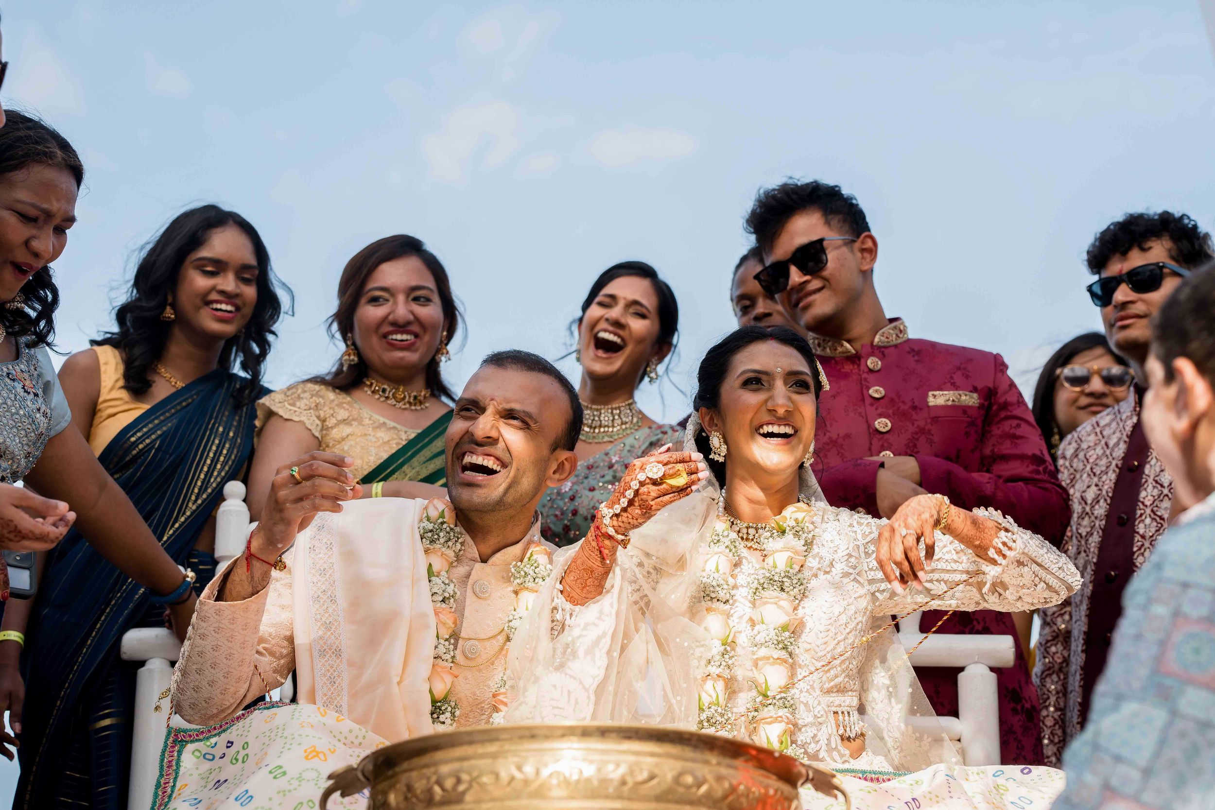 A joyful celebration scene at an outdoor wedding ceremony with guests gathered around a traditional ritual bowl.