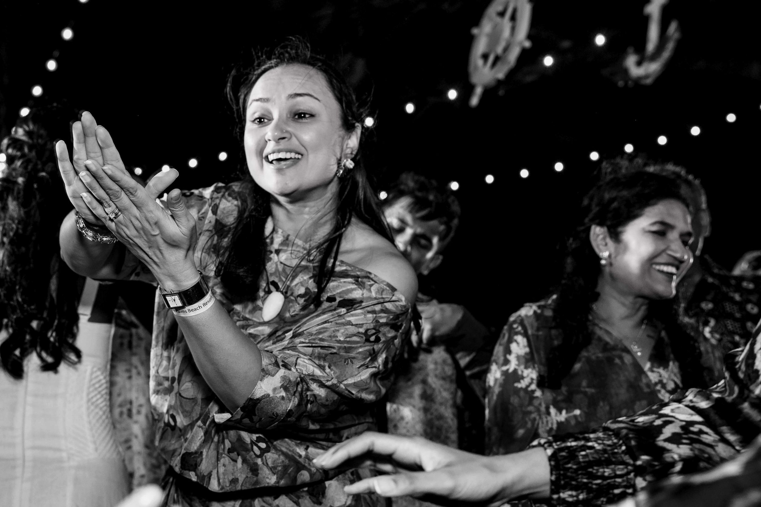 People applaud and celebrate at a nighttime event with string lights overhead in this black and white photograph.