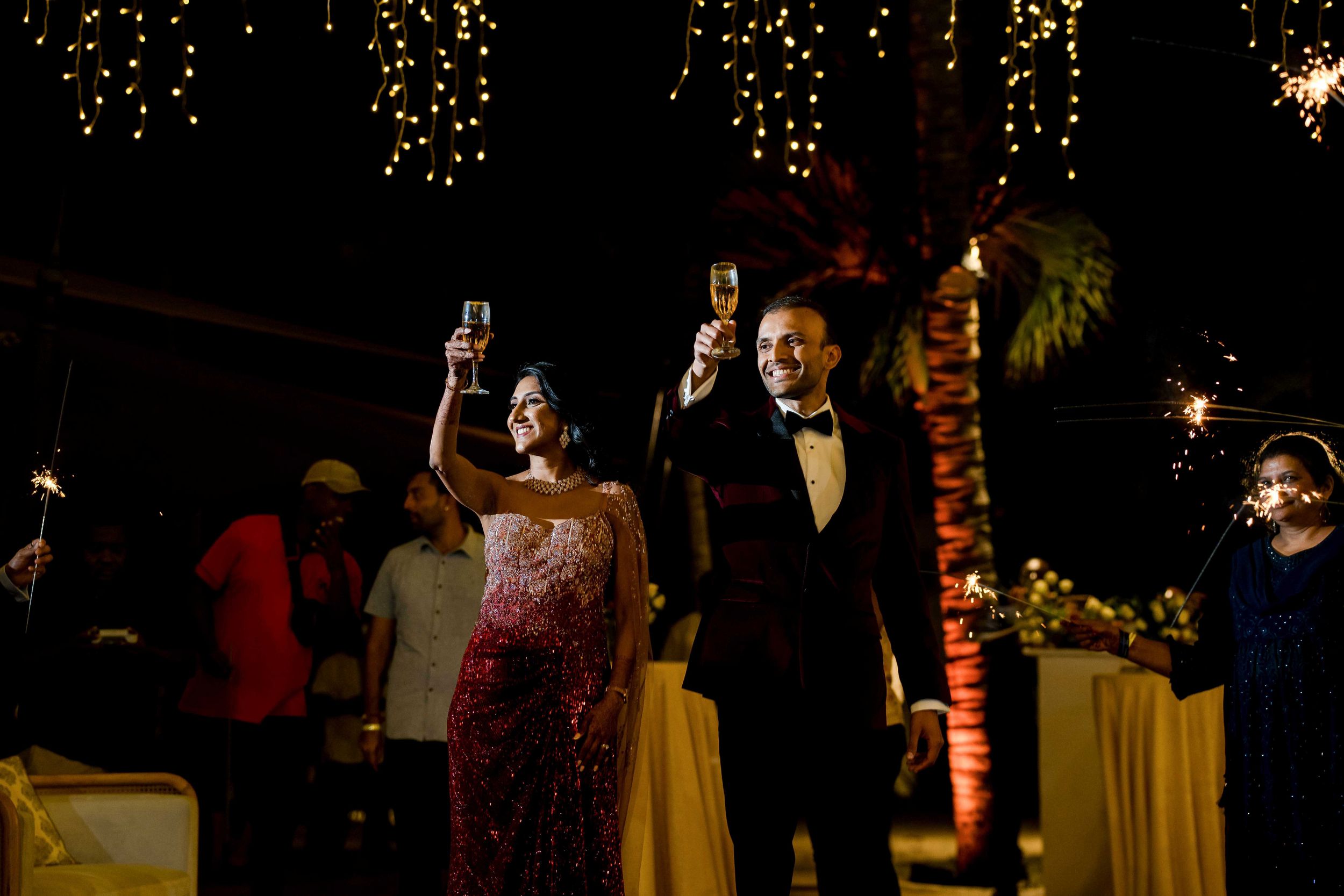 Wedding celebration under glowing light arch as guests applaud during evening reception.