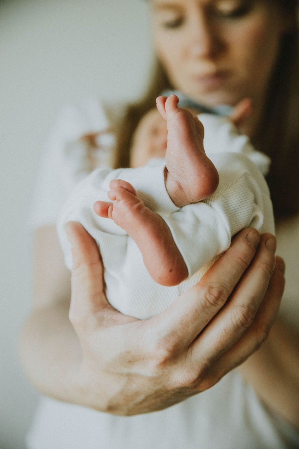 Close-up view of tiny newborn baby feet being gently held by adult hands in soft natural lighting.