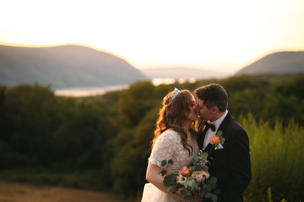 A couple shares a romantic sunset kiss at their wedding with mountains and forest in the background.