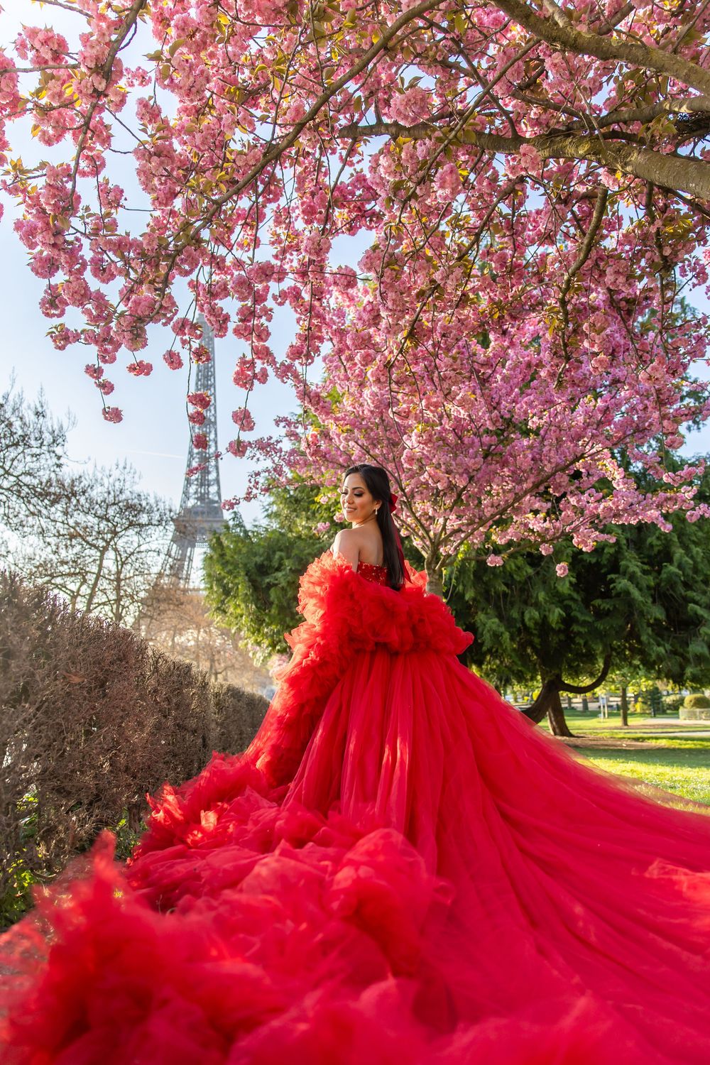 Stunning red tulle gown billowing in the wind beneath pink cherry blossoms with the Eiffel Tower in the background.