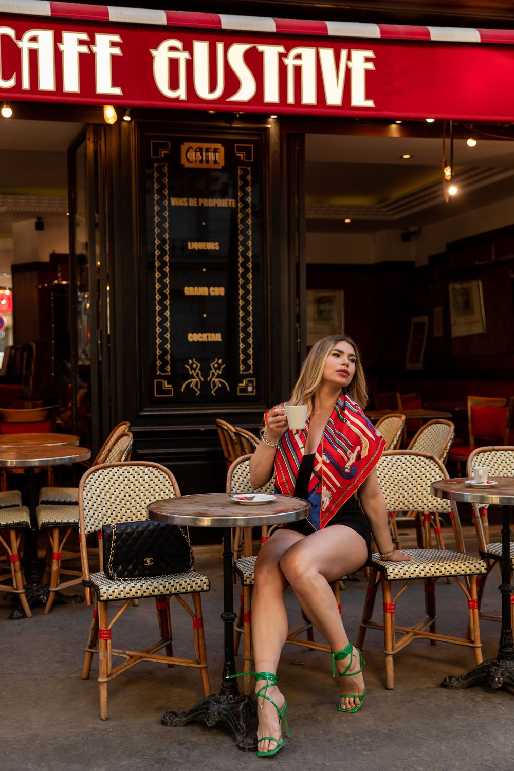 Four part sequence shows person in red dress sitting at Paris cafe with outdoor wicker chairs and vintage storefront sign.