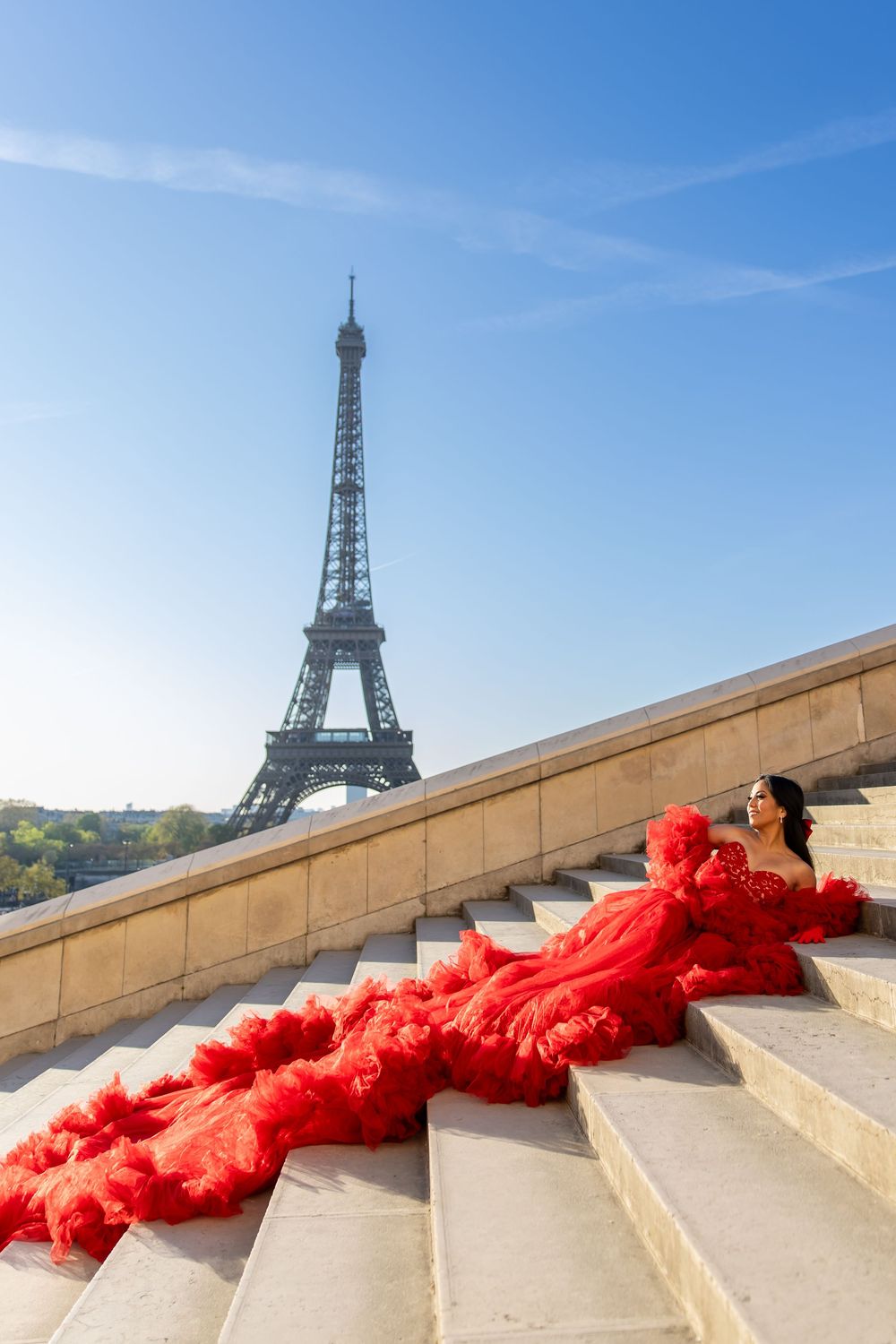A dramatic red flowing dress cascades down stone steps at Trocadero with the Eiffel Tower in the background in Paris.