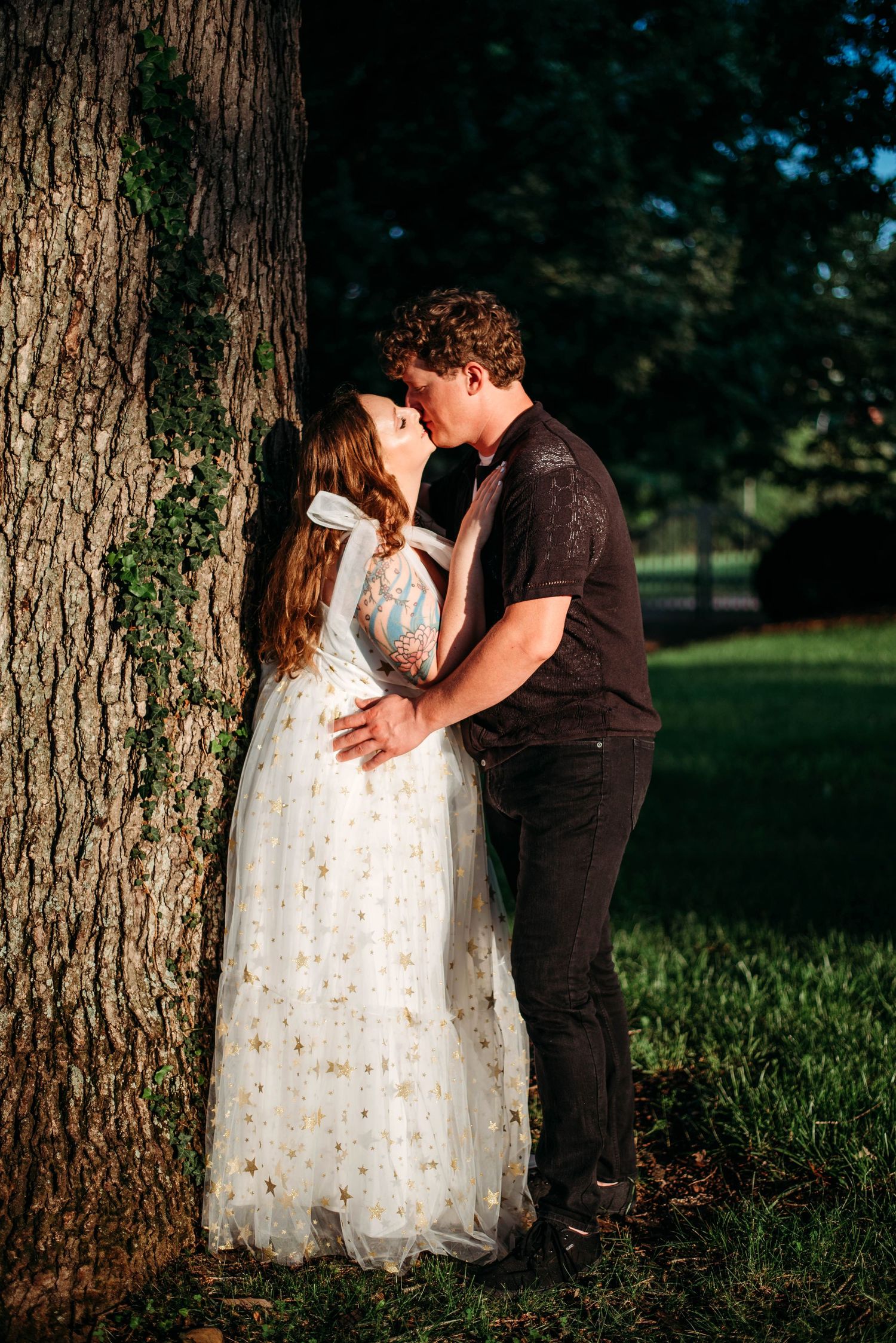 A romantic moment captured by a large tree trunk in evening light. Engagement photoshoot in VA.