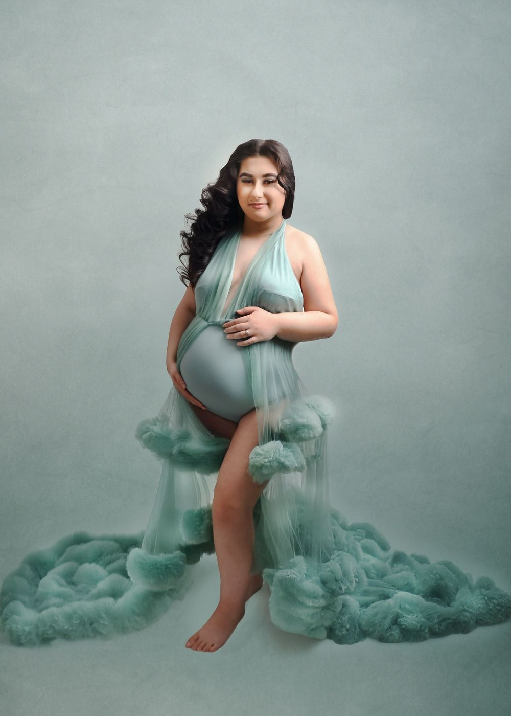Maternity portrait with billowing mint green tulle fabric creating dreamy underwater effect.