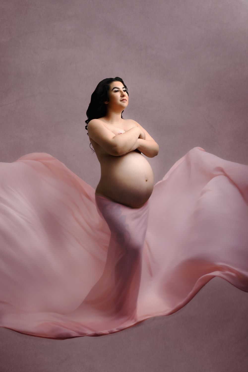 Artistic pregnancy photo with billowing pink silk fabric creating dynamic movement.