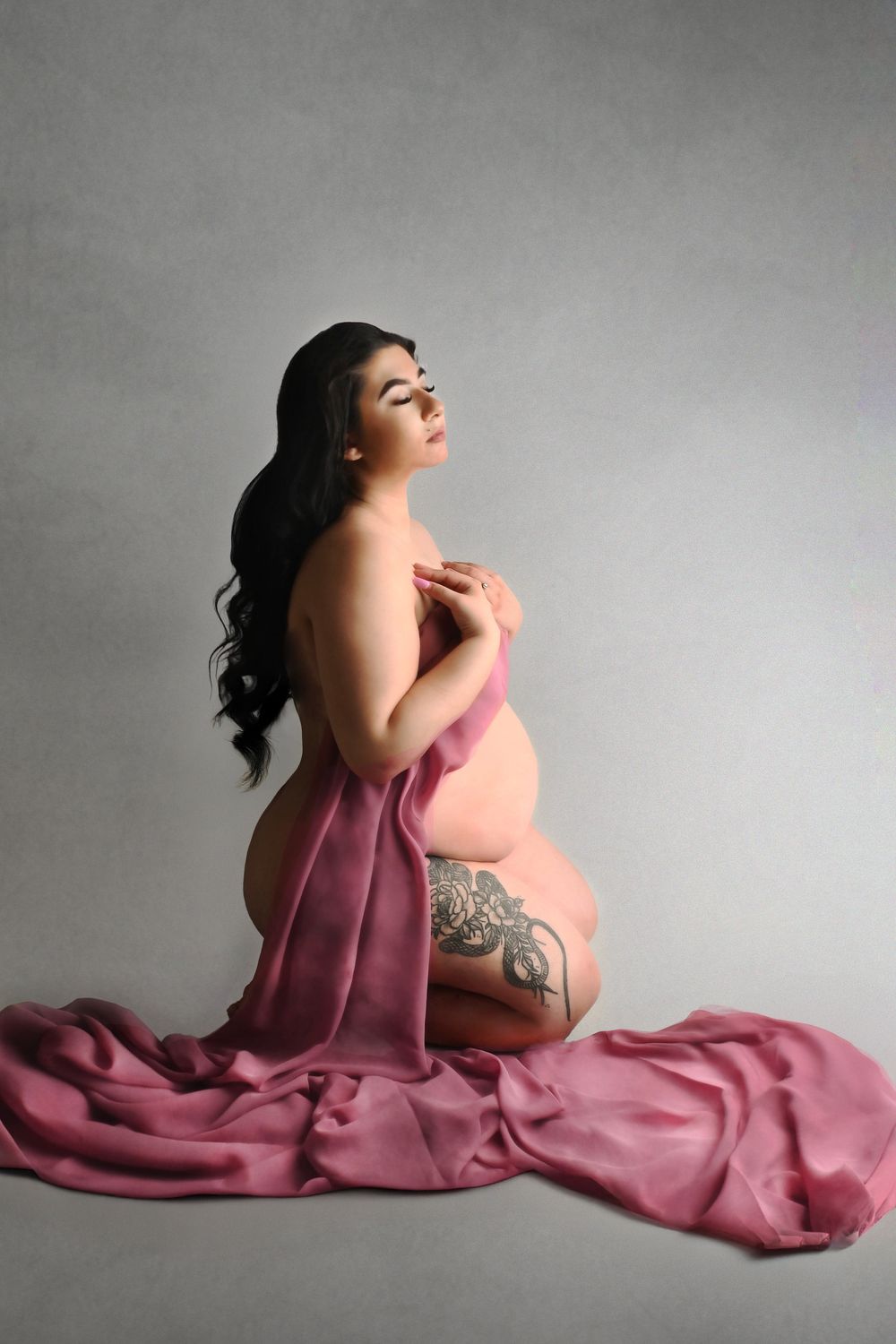 Artistic maternity portrait with burgundy fabric draping against light grey backdrop.