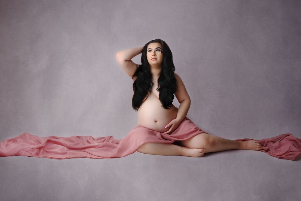 Artistic maternity portrait with pink fabric creating horizontal lines against neutral backdrop.