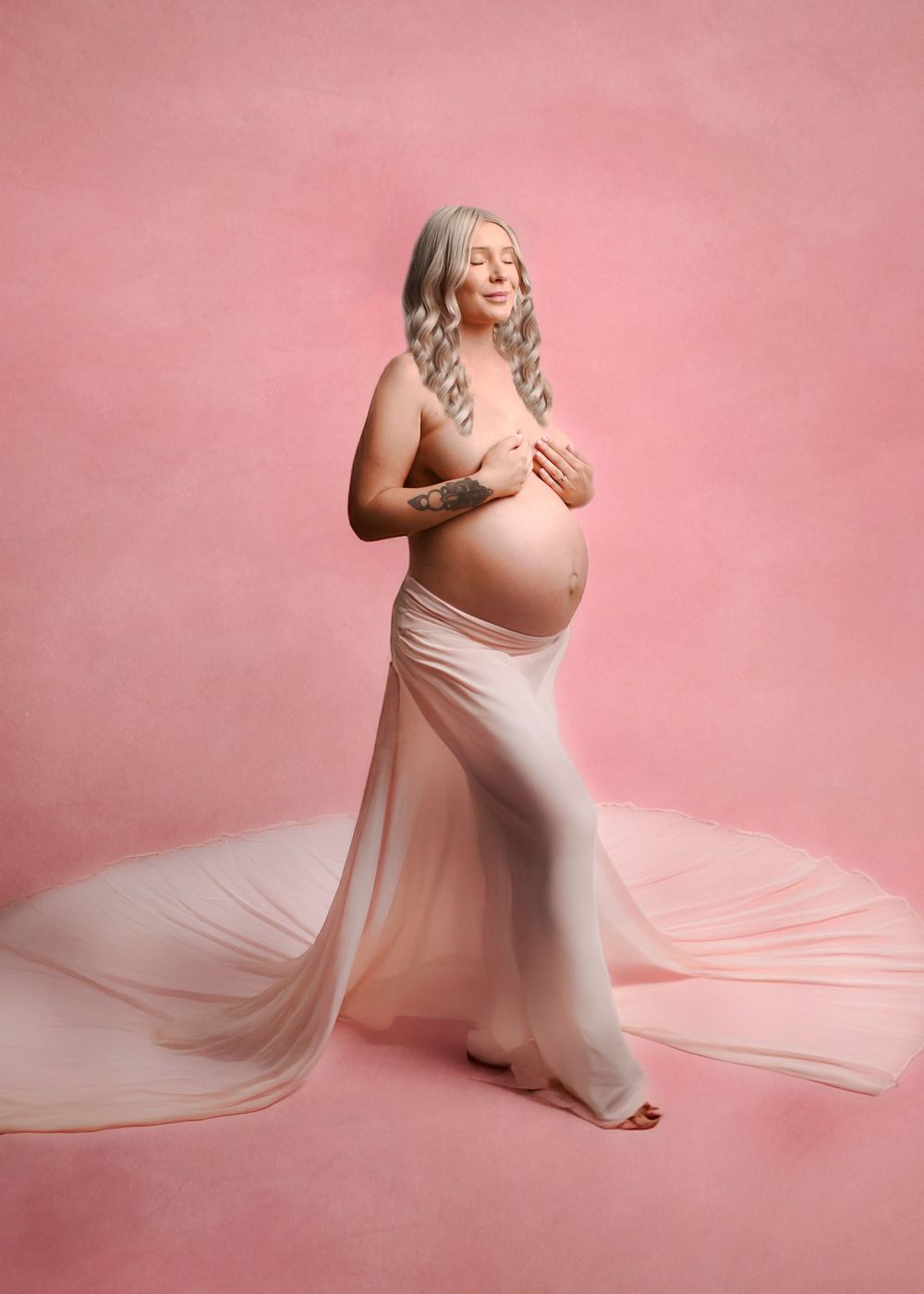 Pregnancy photoshoot featuring soft pink backdrop with flowing fabric creating elegant silhouettes.